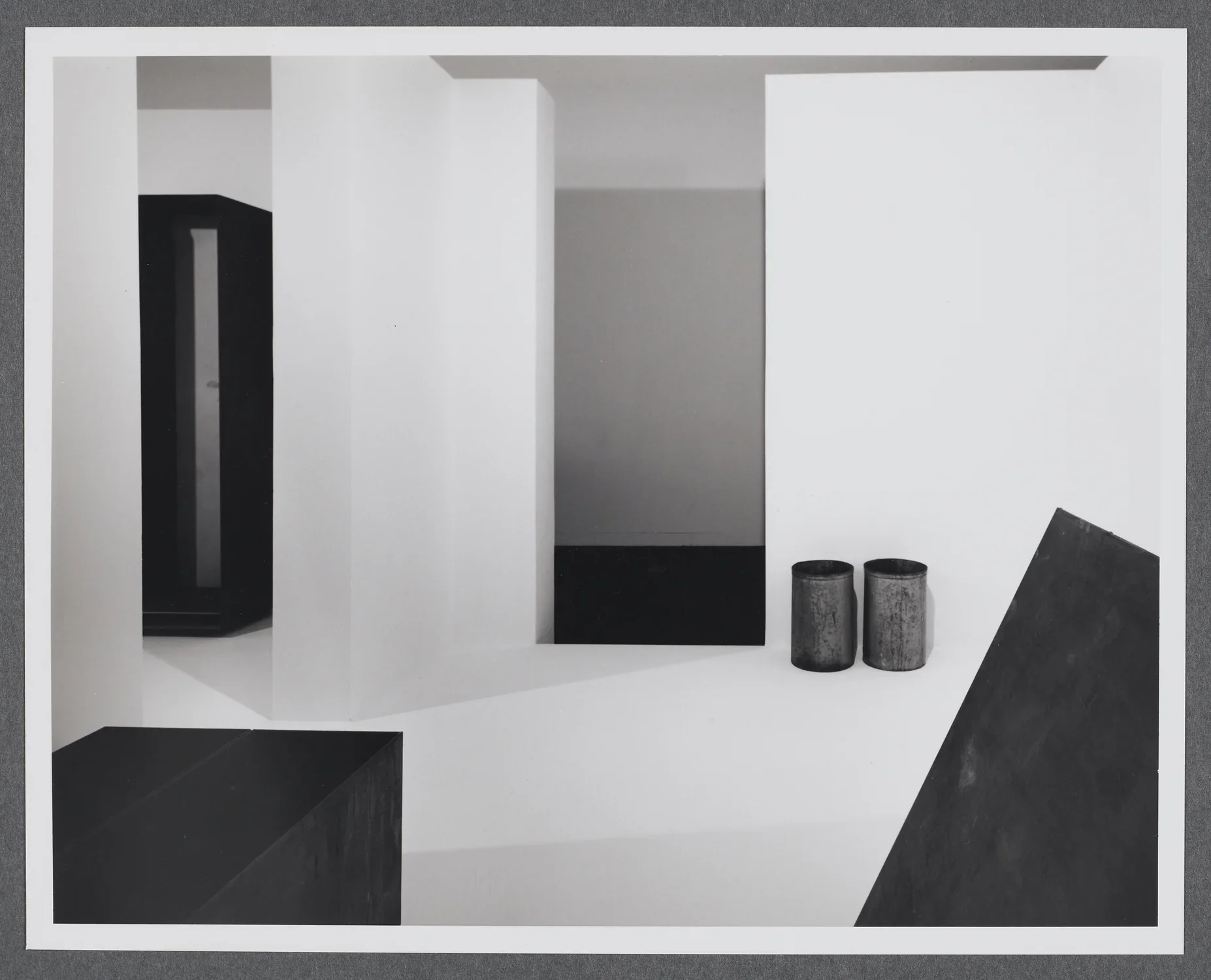 Steel sculptures are displayed in a wite room. Each are geometric forms such as rectangular prisms and cylinders.