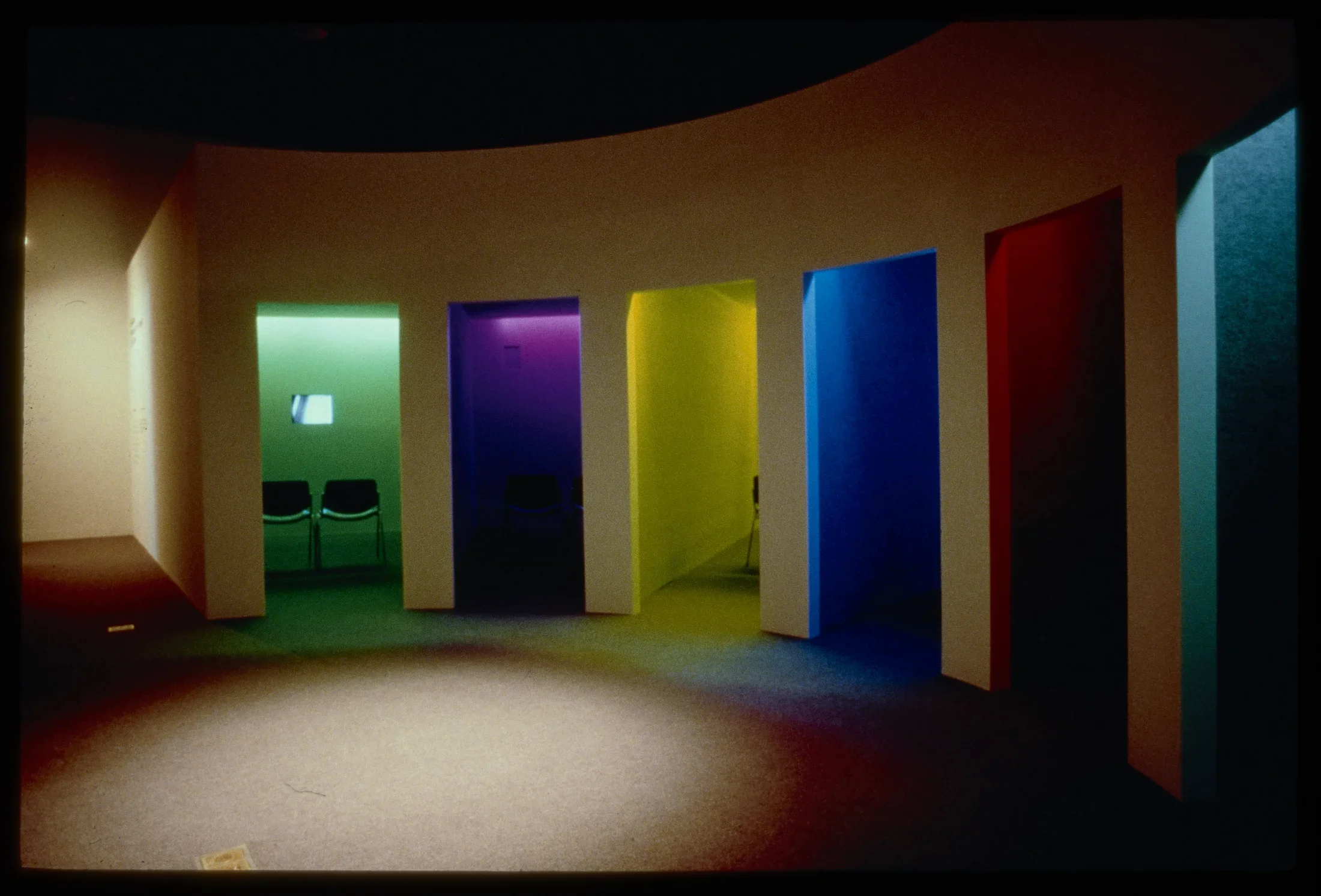 A large segmented structure with a central common space opens into several separate rooms with video monitors. 
