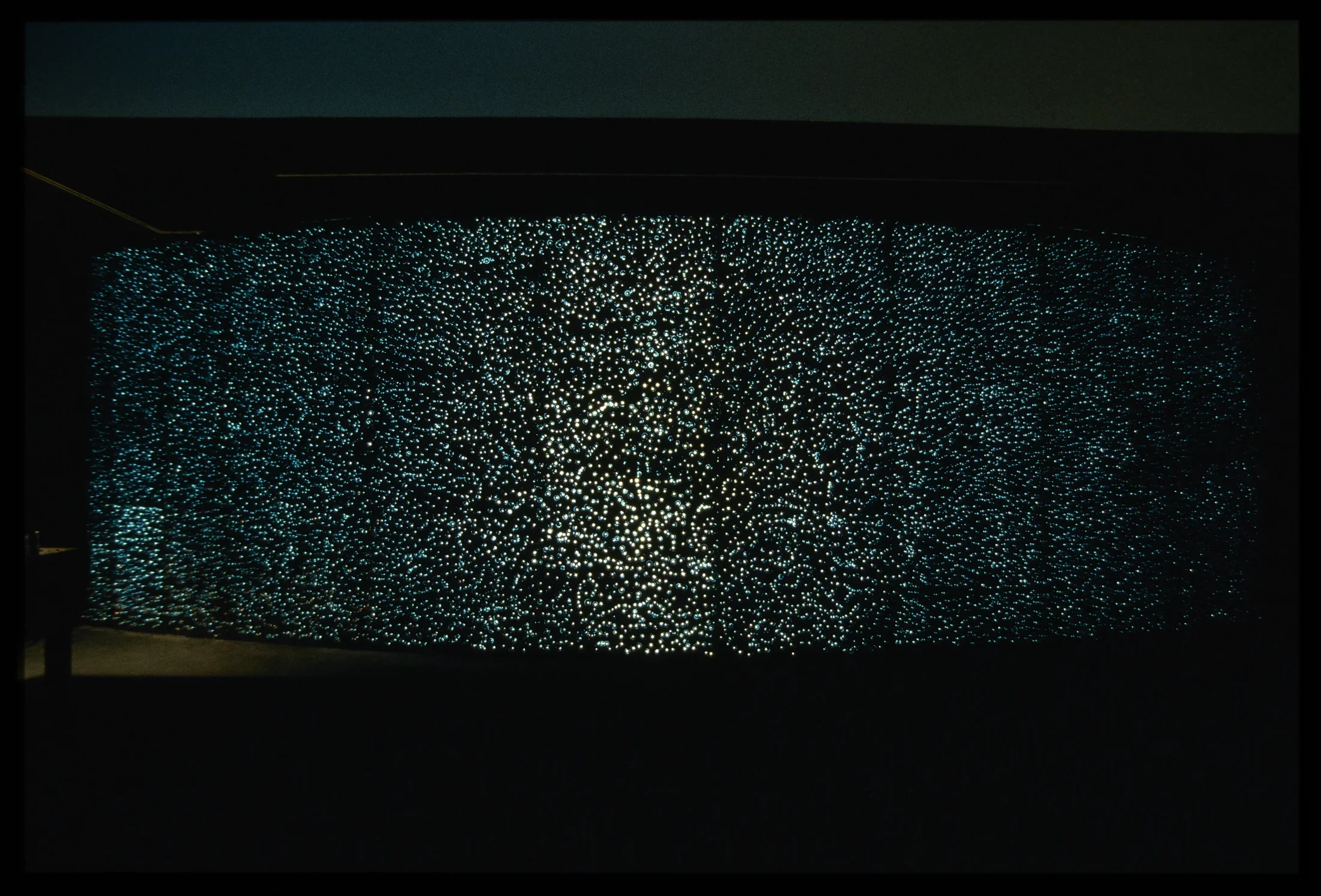 Panels of backlit glass bubbles create a large sparkling wall, bowing outward, in a dark space.