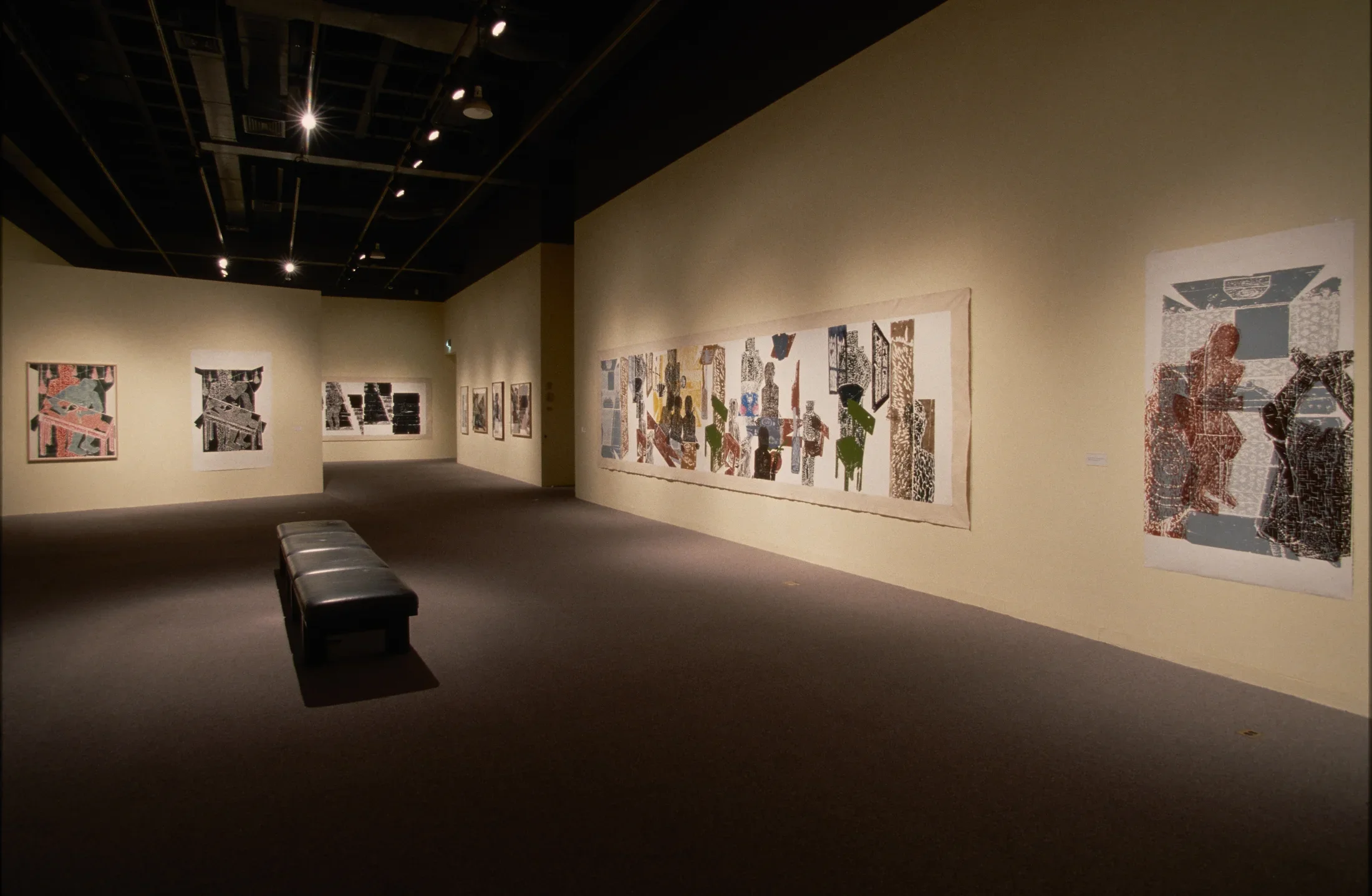 Large, muted-color woodblock prints hang on cream-color walls of a long gallery with a bench in the center for visitors 