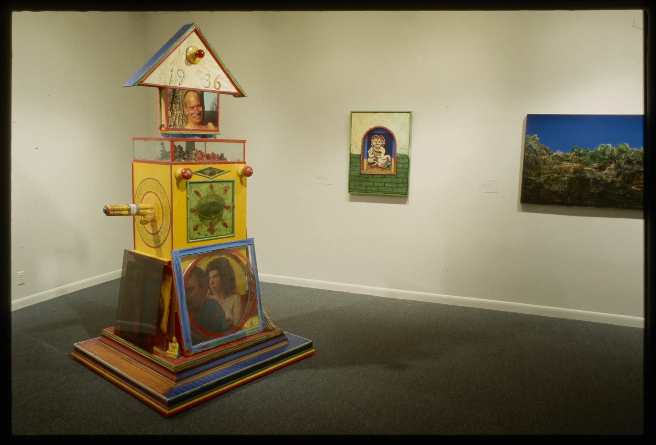 A large yellow sculpture is in the foreground with 2 paintings on the back wall of the gallery.