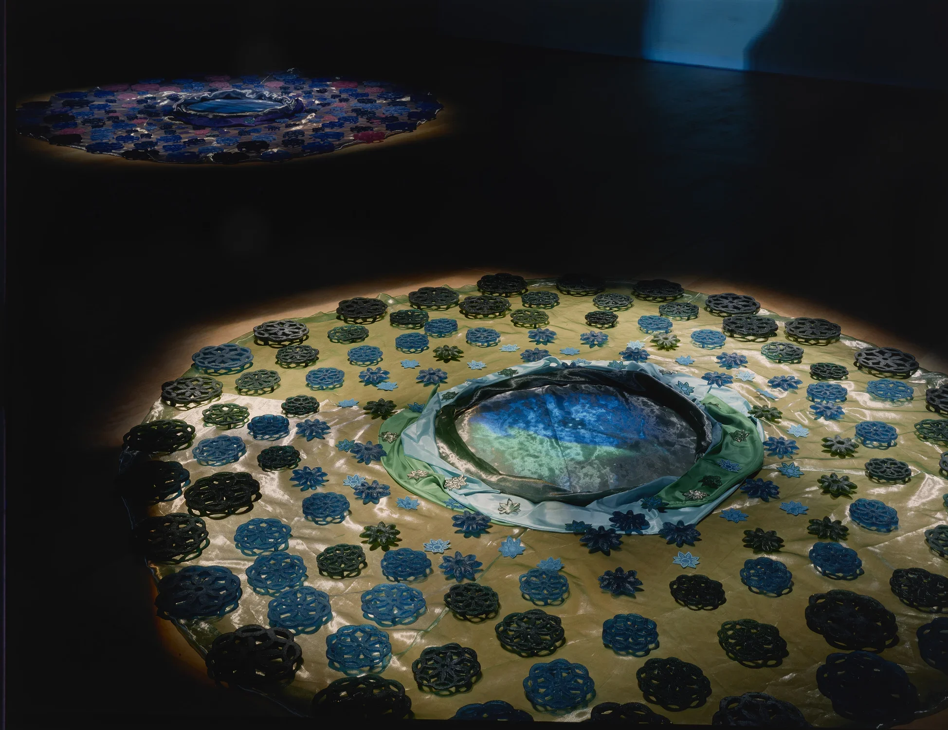 A group of large and small, blue and pink cast-glass flower shapes on pink-cream, shiny organza fabric