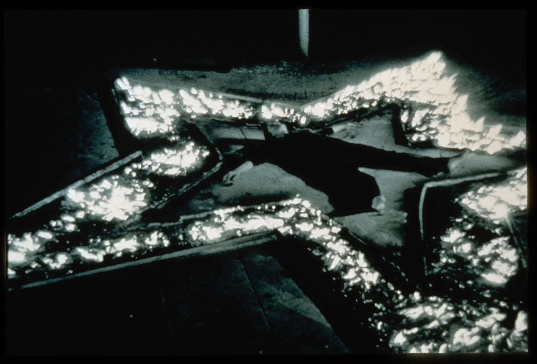 A monochrome image of a person lying face up, arms out, legs splayed, inside the brightly lit outline of a star on the ground.
