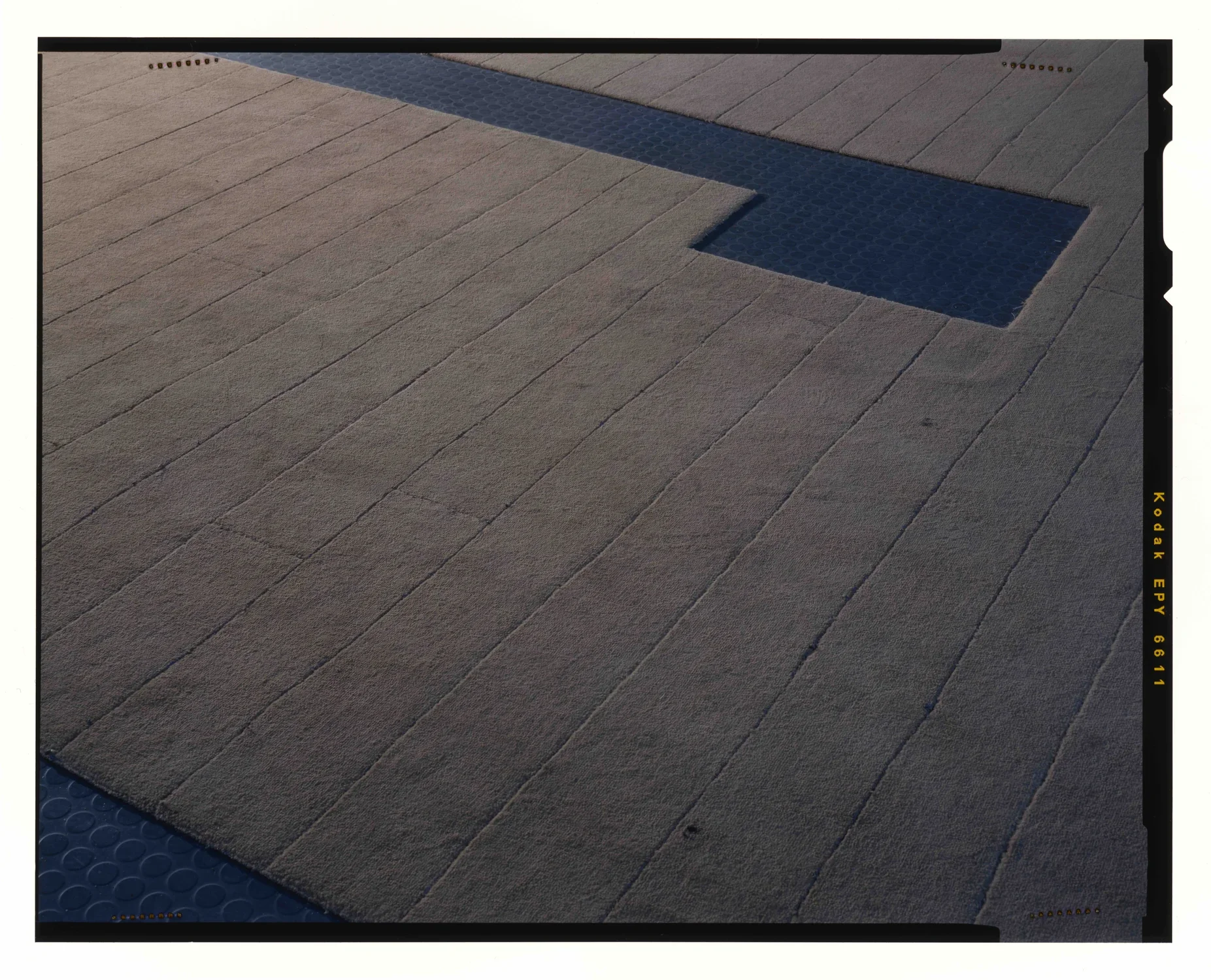 Shaved tan carpet with a long rectilinear cutout shows the dark rubber flooring underneath.