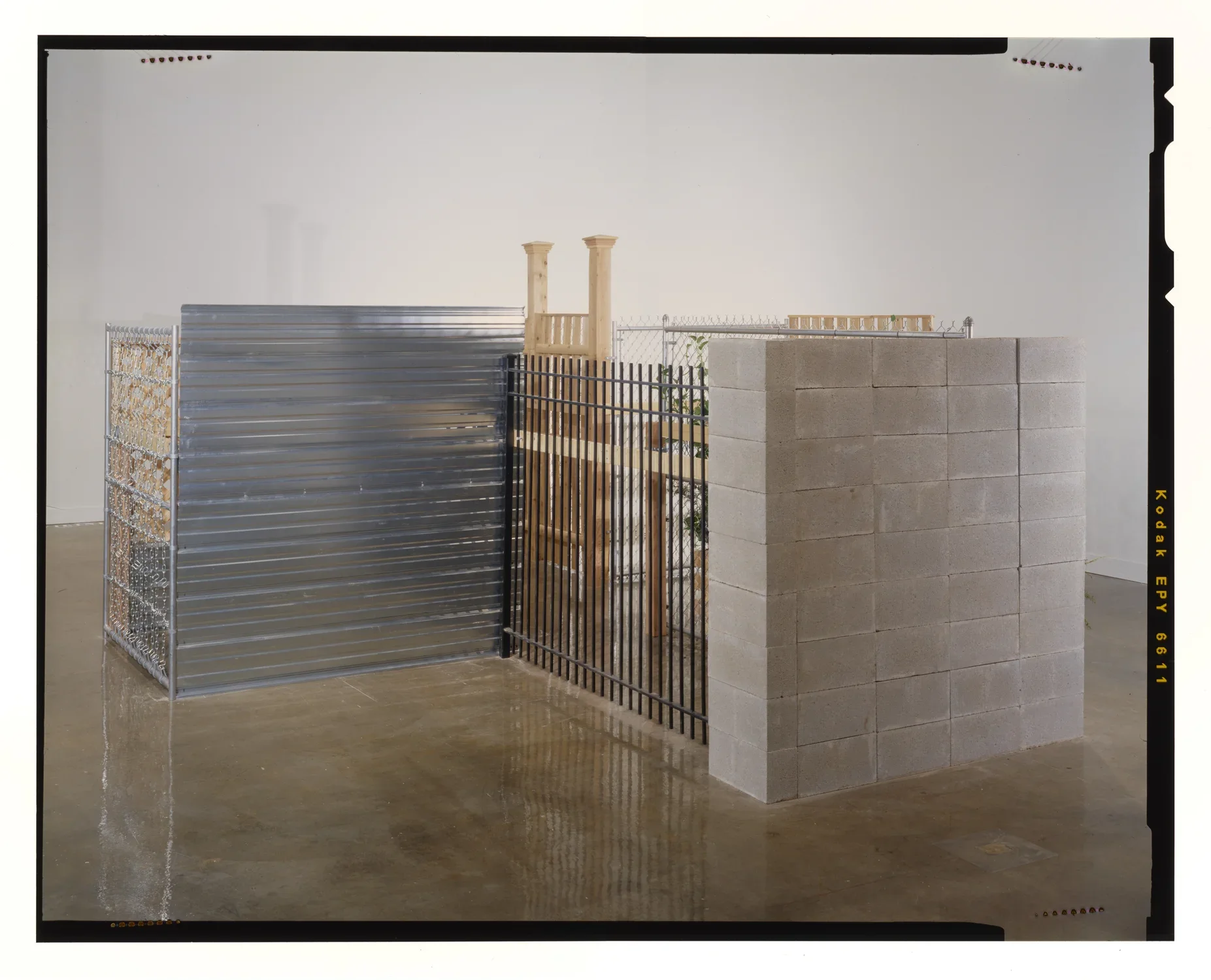 An enclosure of varying materials, including chain-link, high wooden boards, sheet metal, and a concrete colored block wall.