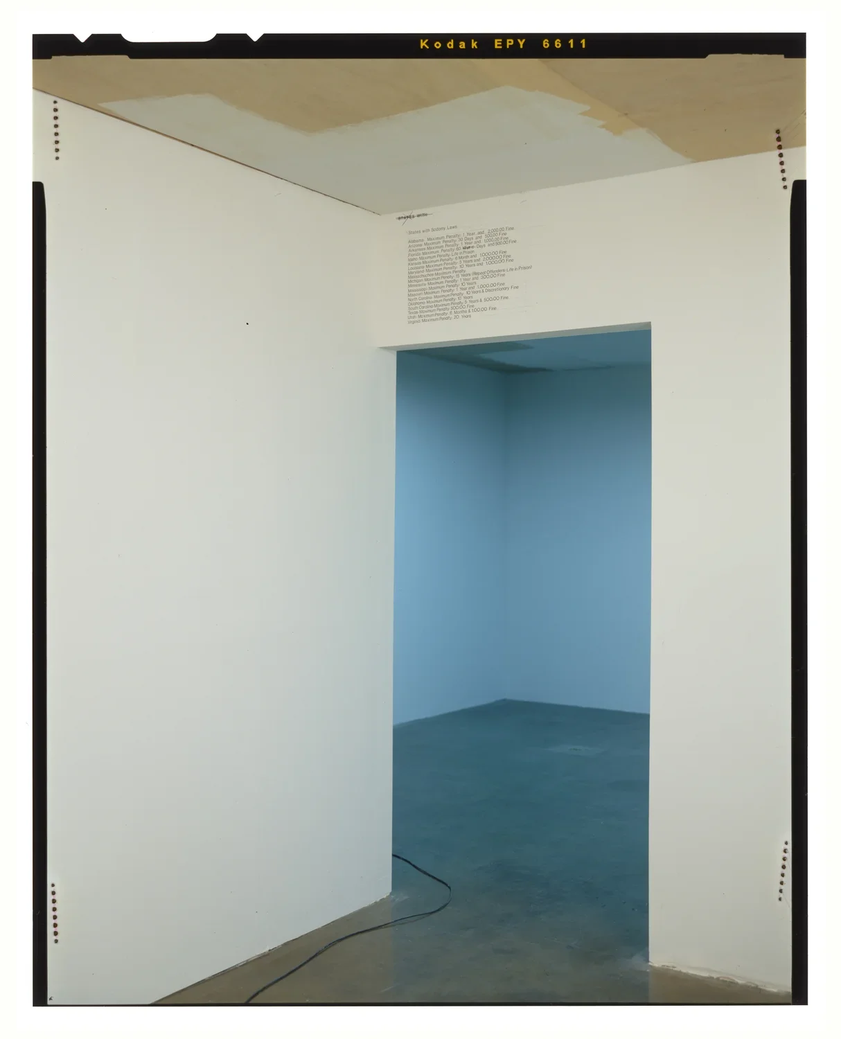 A room with a partially painted ceiling, opens to another room, dimly lit. An electrical cord snakes between the 2 spaces.