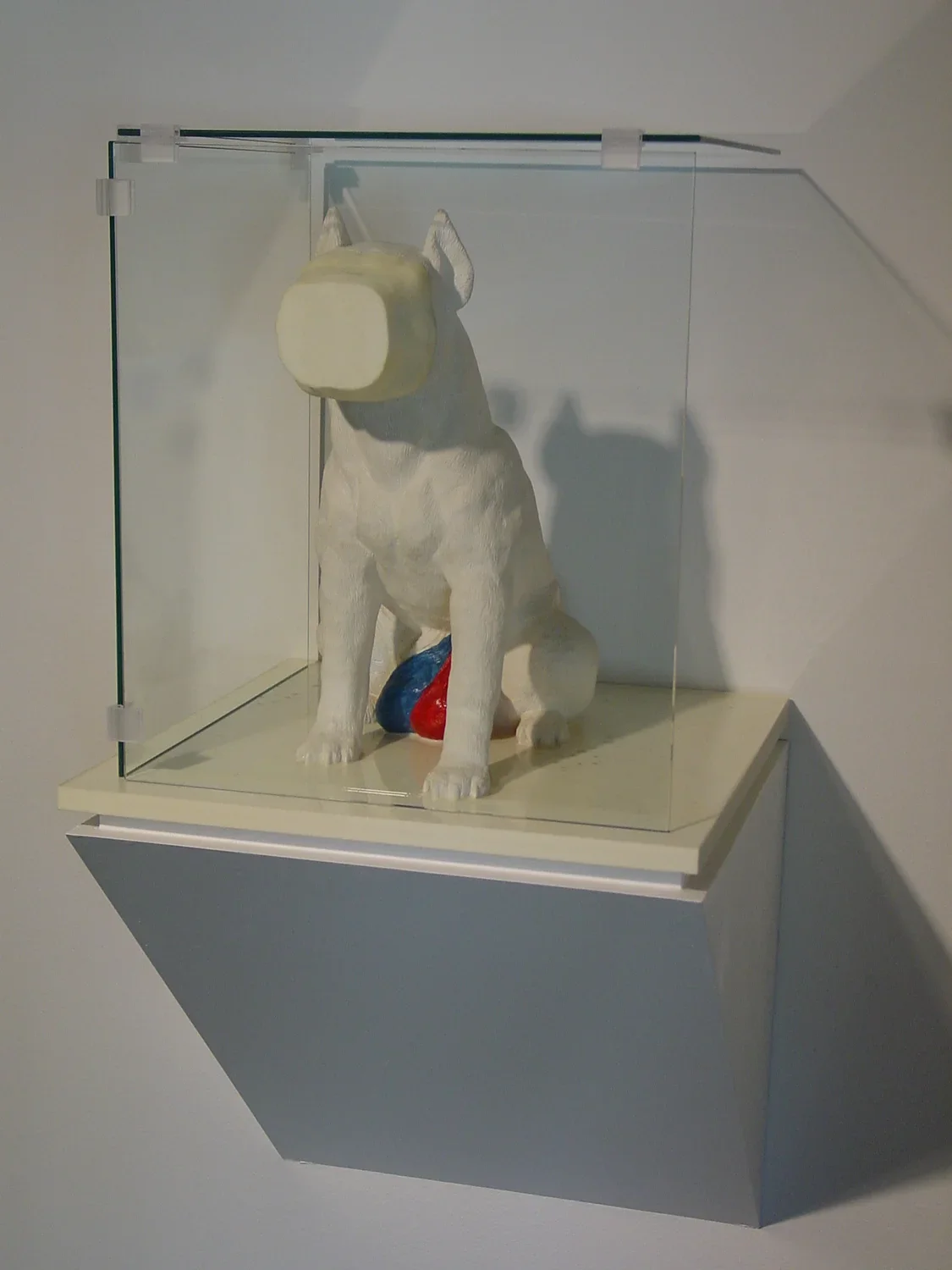 Mounted to the wall, a glass vitrine holds plaster statue of a seated dog with a flattened face
