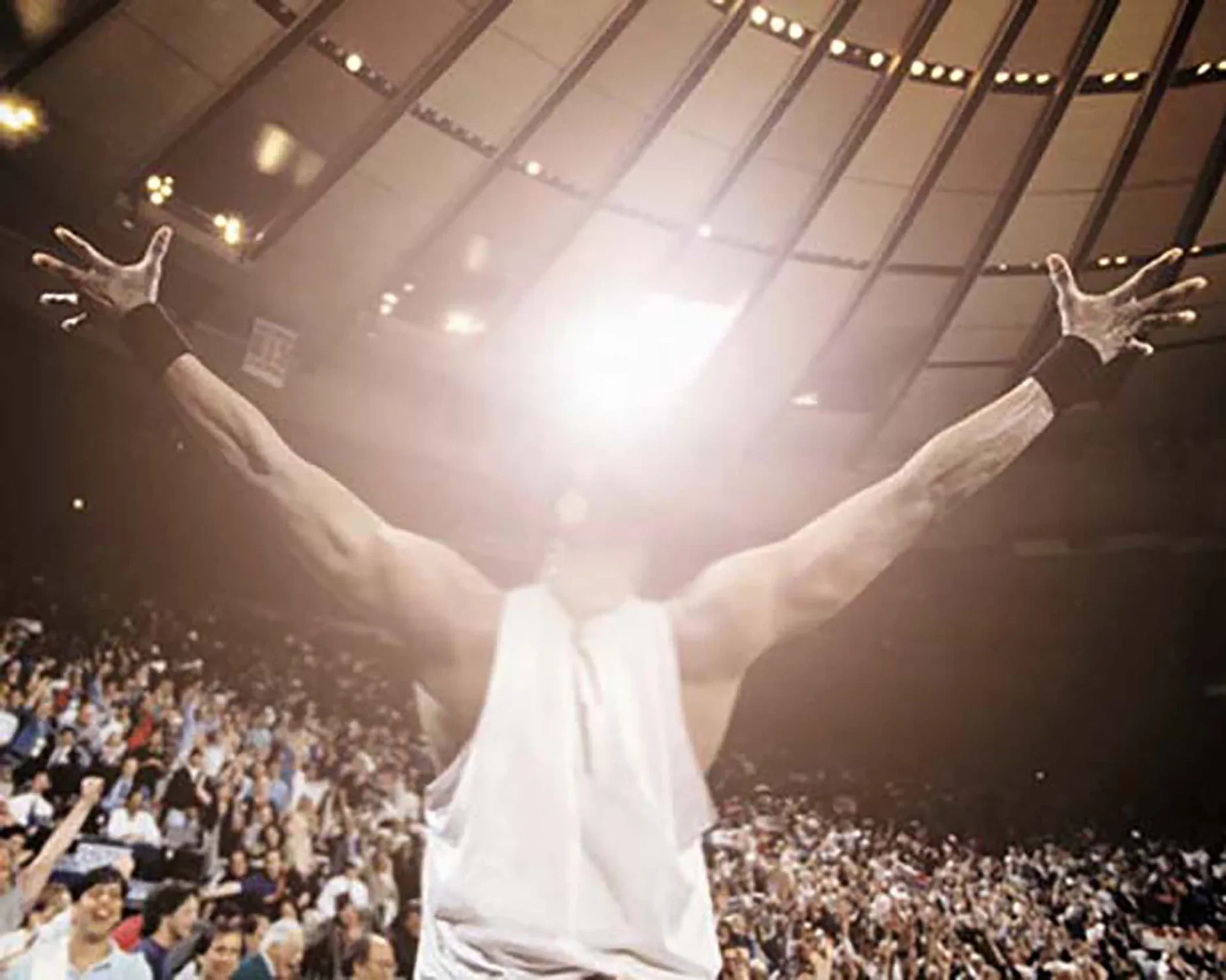 Photograph of a crowded sports arena cheering around an athlete with his arms outstretched