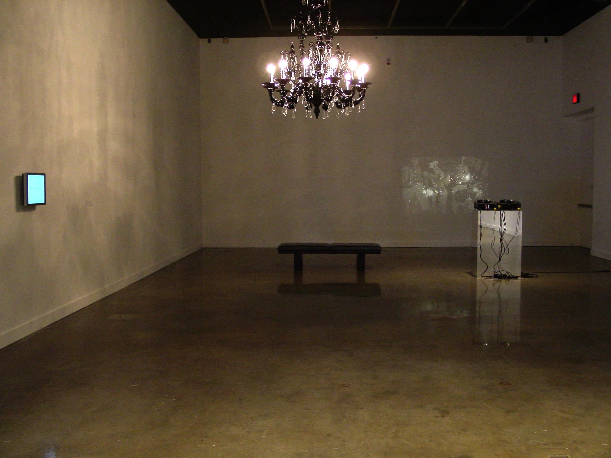 View of a large mirrored sculpture reflecting the gallery upside down and 3 scholar’s rocks on pedestals under glass cases. 