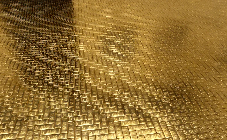A shiny golden floor made from small sculptures which resemble bars of gold arranged in a brickwork pattern.