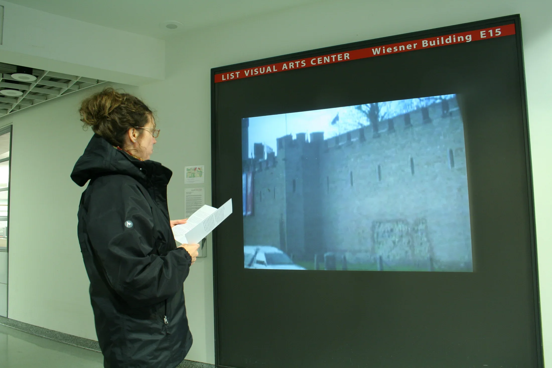 A visitor stands in front of video projection in a hallway showing a structure that has walls like a castle.