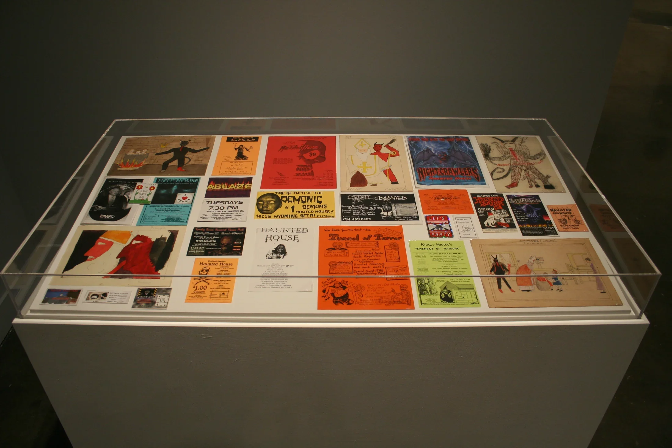Birds-eye view of glass case displaying colorful Haunted House fliers made of various media, & sketches for scary creatures