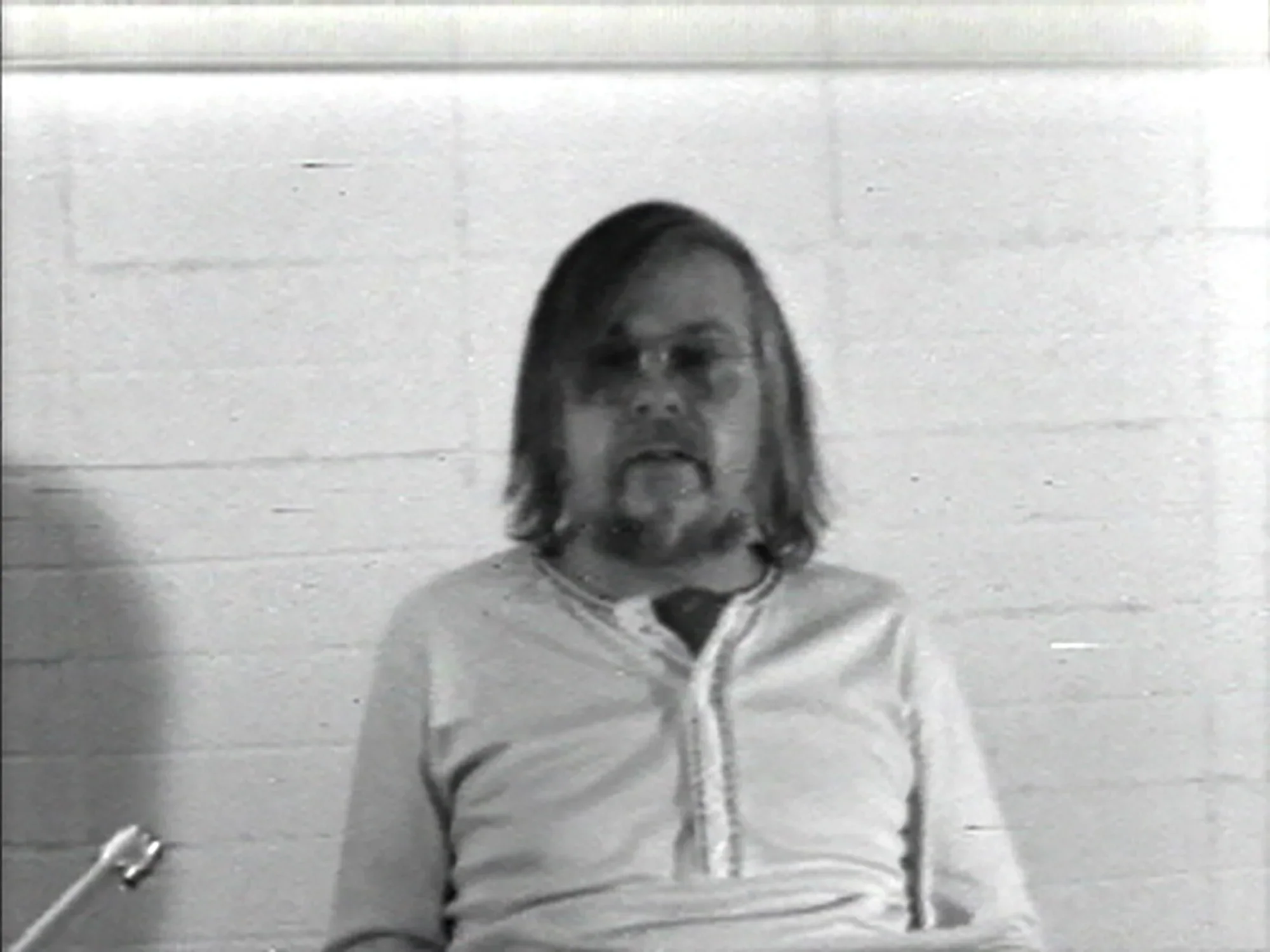 Man sitting in front of a cement wall with a microphone in the front left corner. 