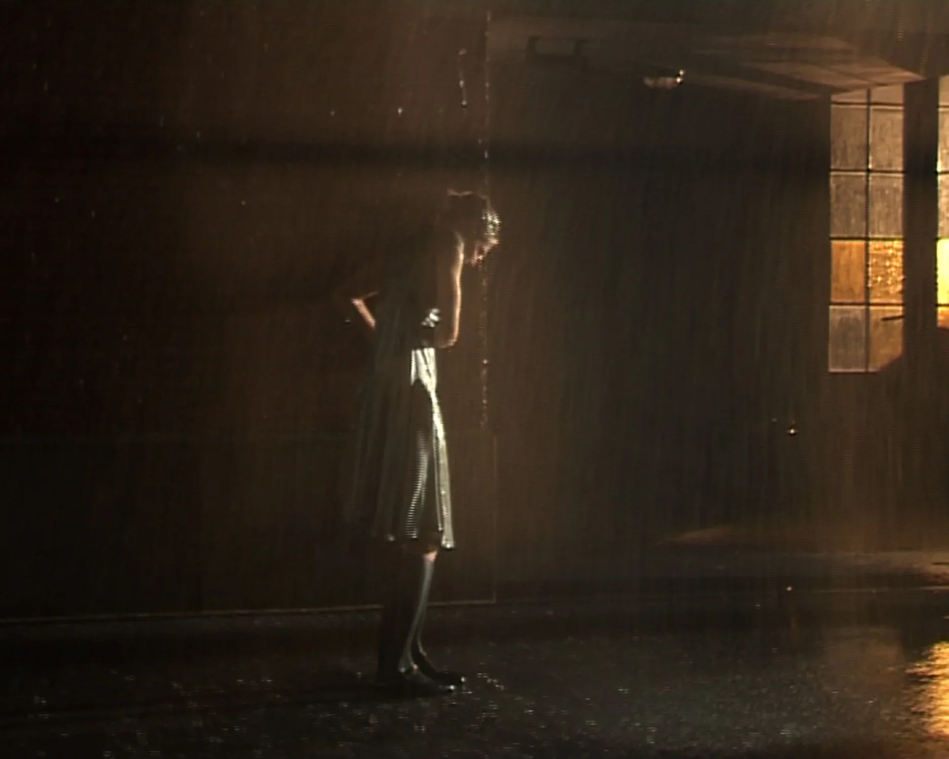 Video still of a woman standing outside in the pouring rain dressed in a light sun dress. 