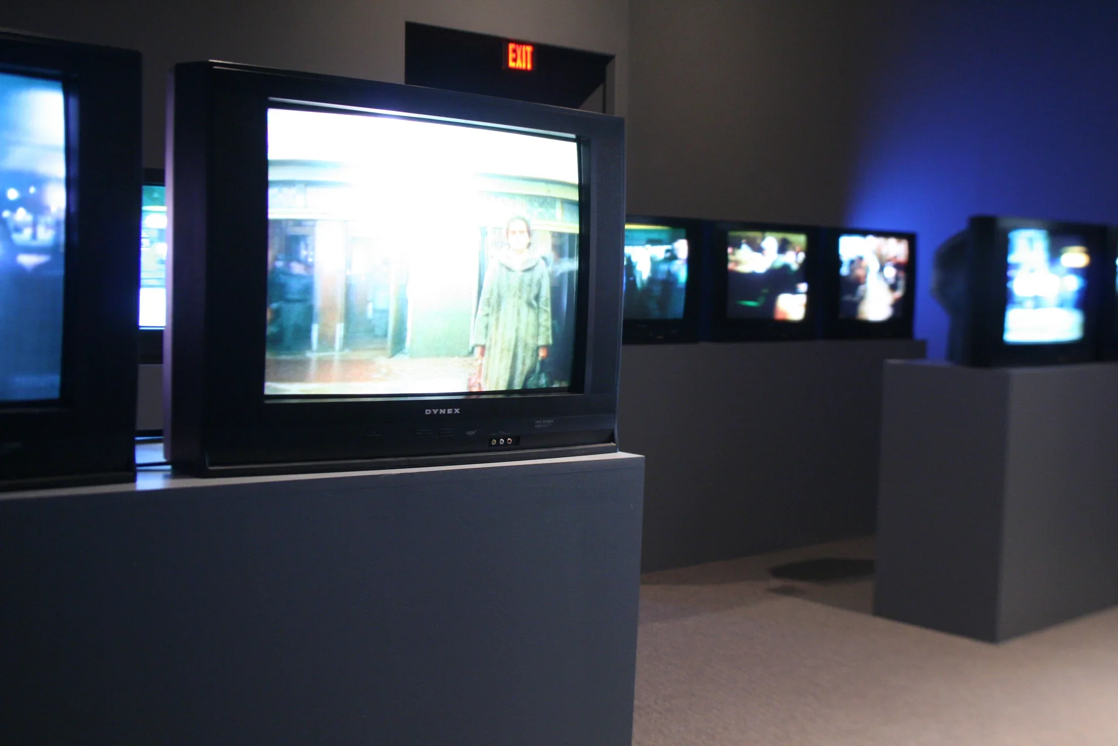 Many screens installed on podiums in a darkened gallery. 
