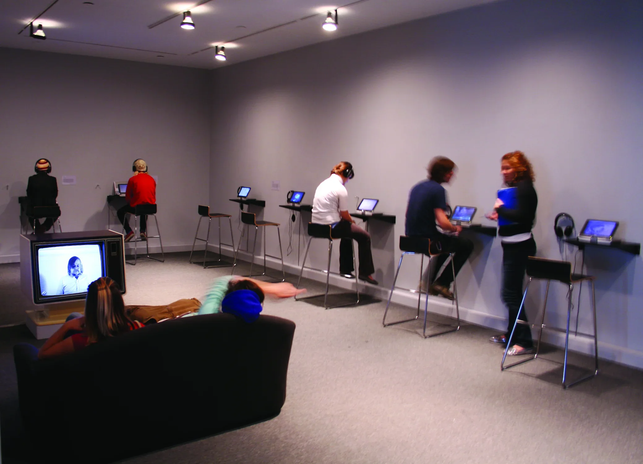 Visitors in a museum space looking at the TVs screens on view. 