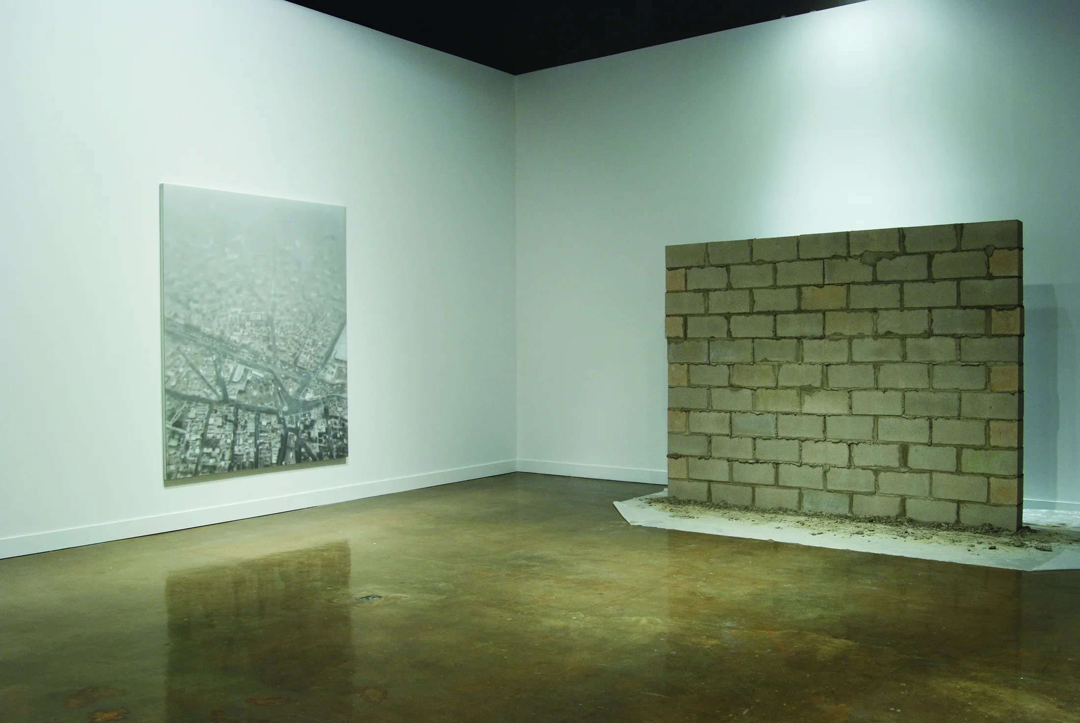 A large black and white aerial view of a city on one wall, and a standing wall of concrete bricks in front of the other wall