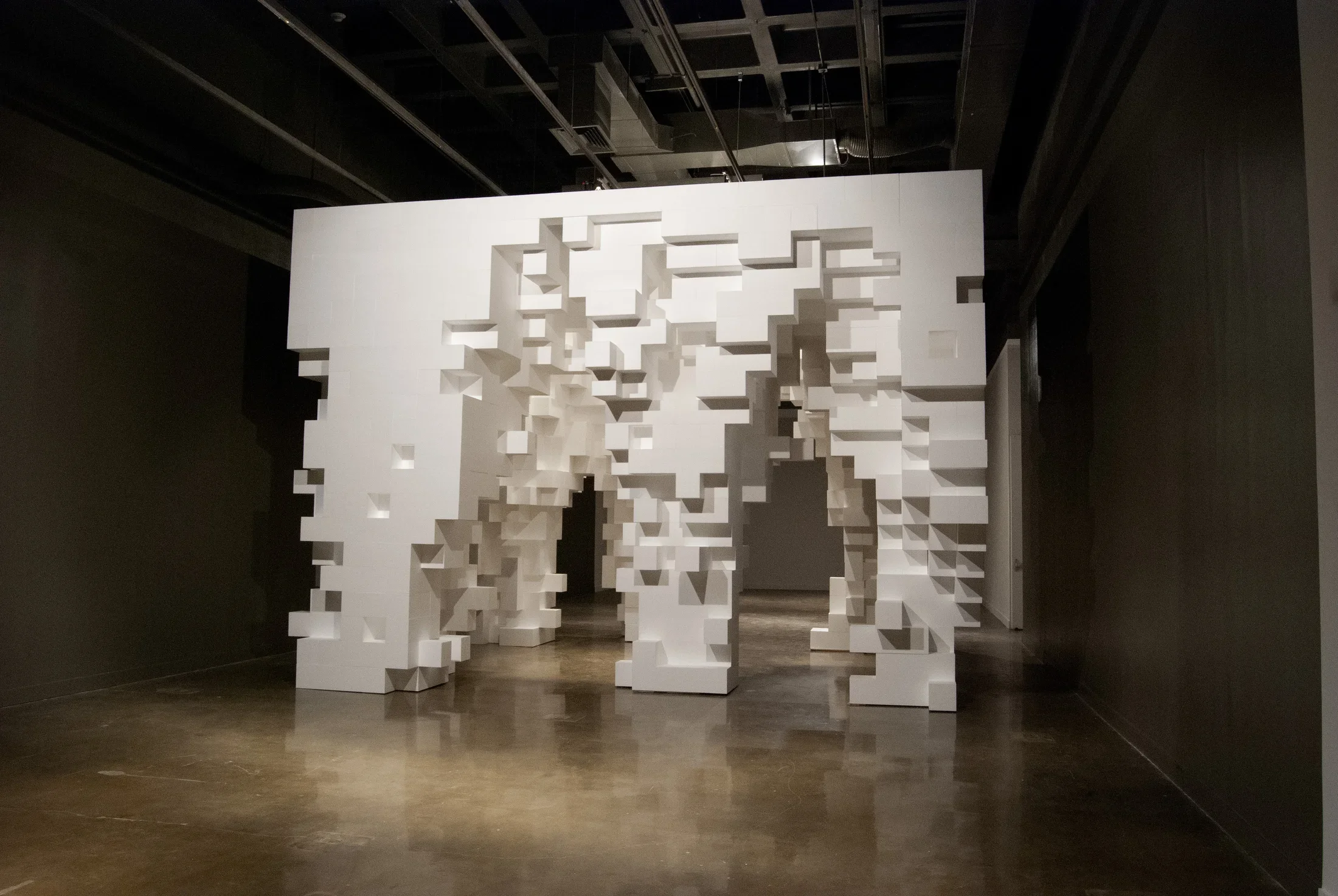 Cube-like structure made from white Styrofoam blocks and blocks removed to form irregular-shaped arch openings and footings