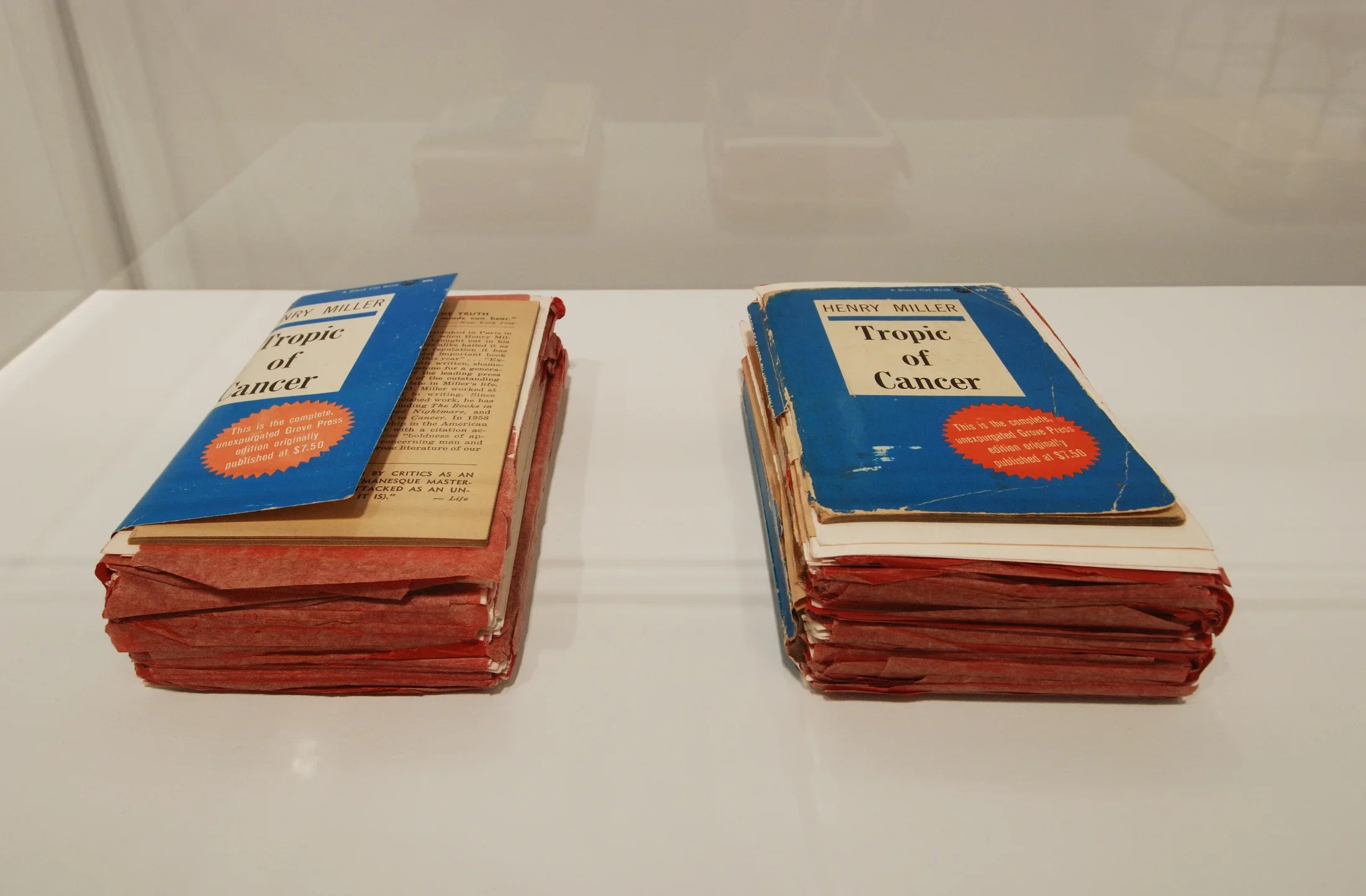 Two copies of Henry Miller's "Tropic of Cancer" sit side by side. They are both well worn and filled with red note cards indicating annotations. 