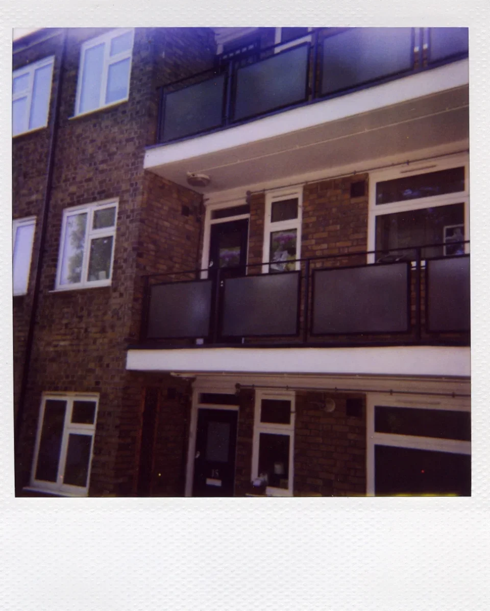 Close-up view of a 3-story brick building with white mullion windows and balconies on the 2nd and 3rd floors.