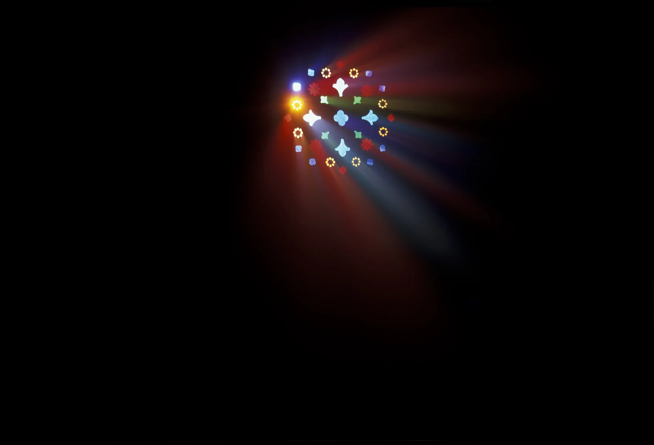 Red, blue and gold rays of light stream through the multicolor shapes of a stain-glass window against a black background.