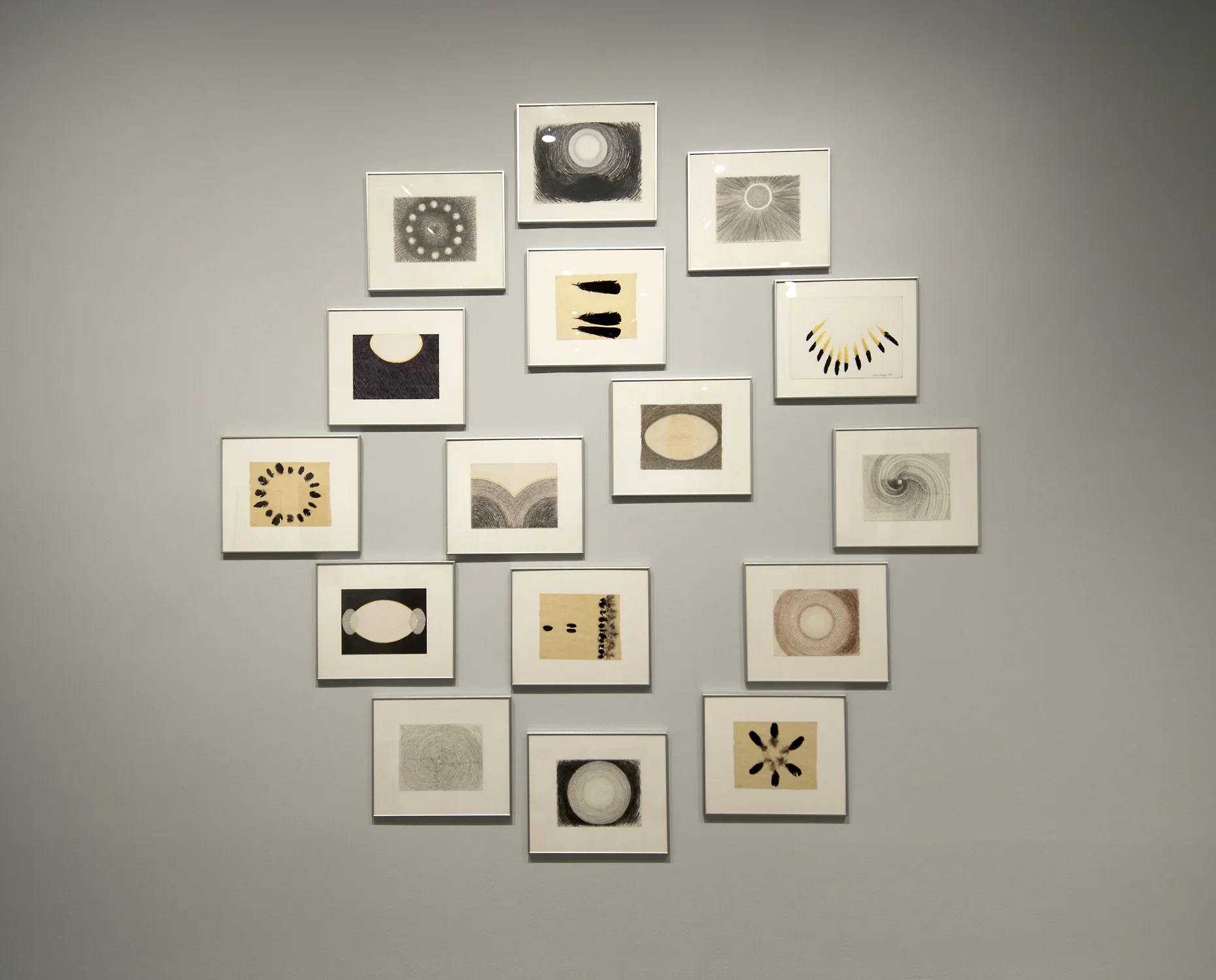 16 works of art framed and hung in a large circle.