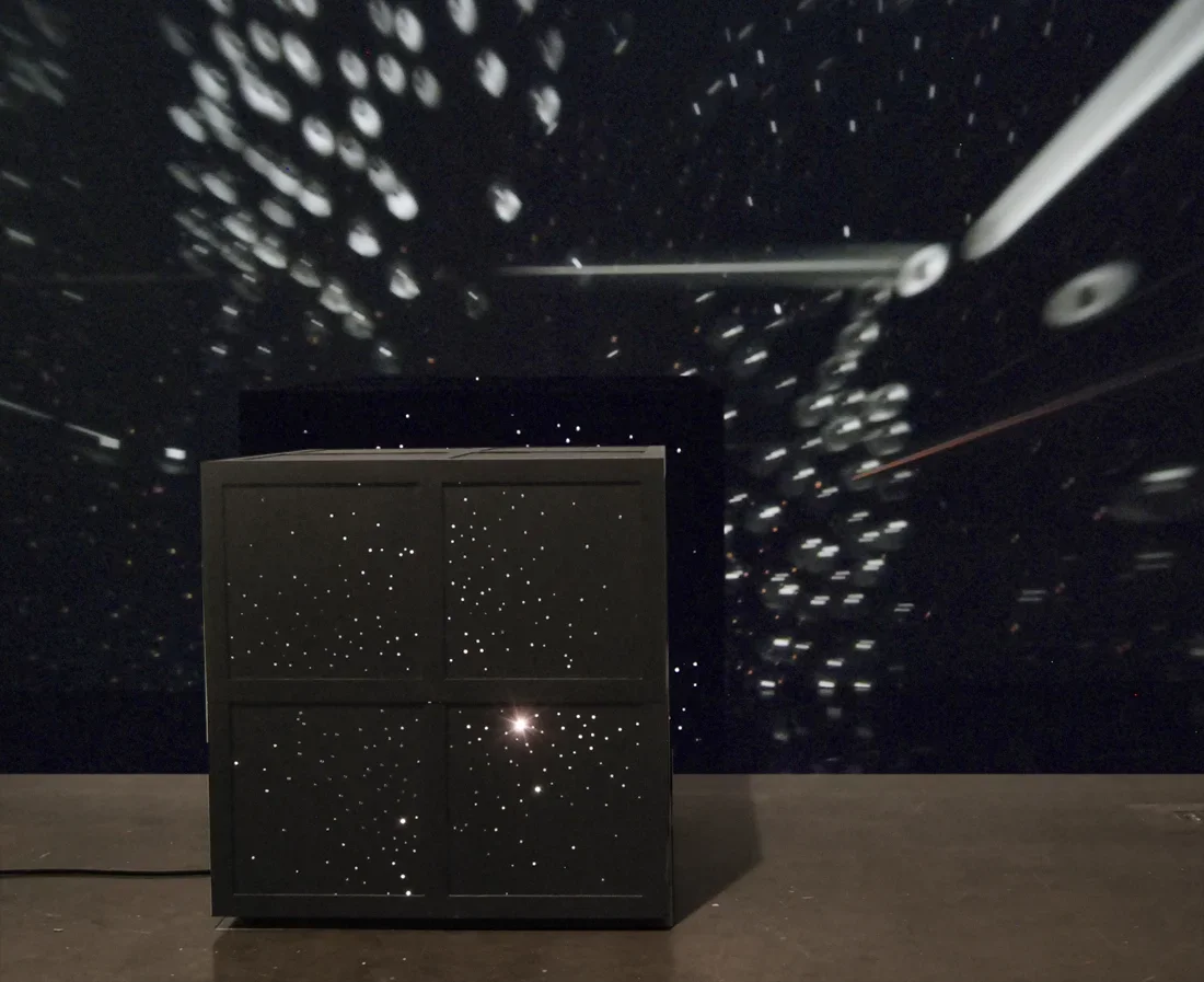 A large black square rests on the floor with light emanating from within.