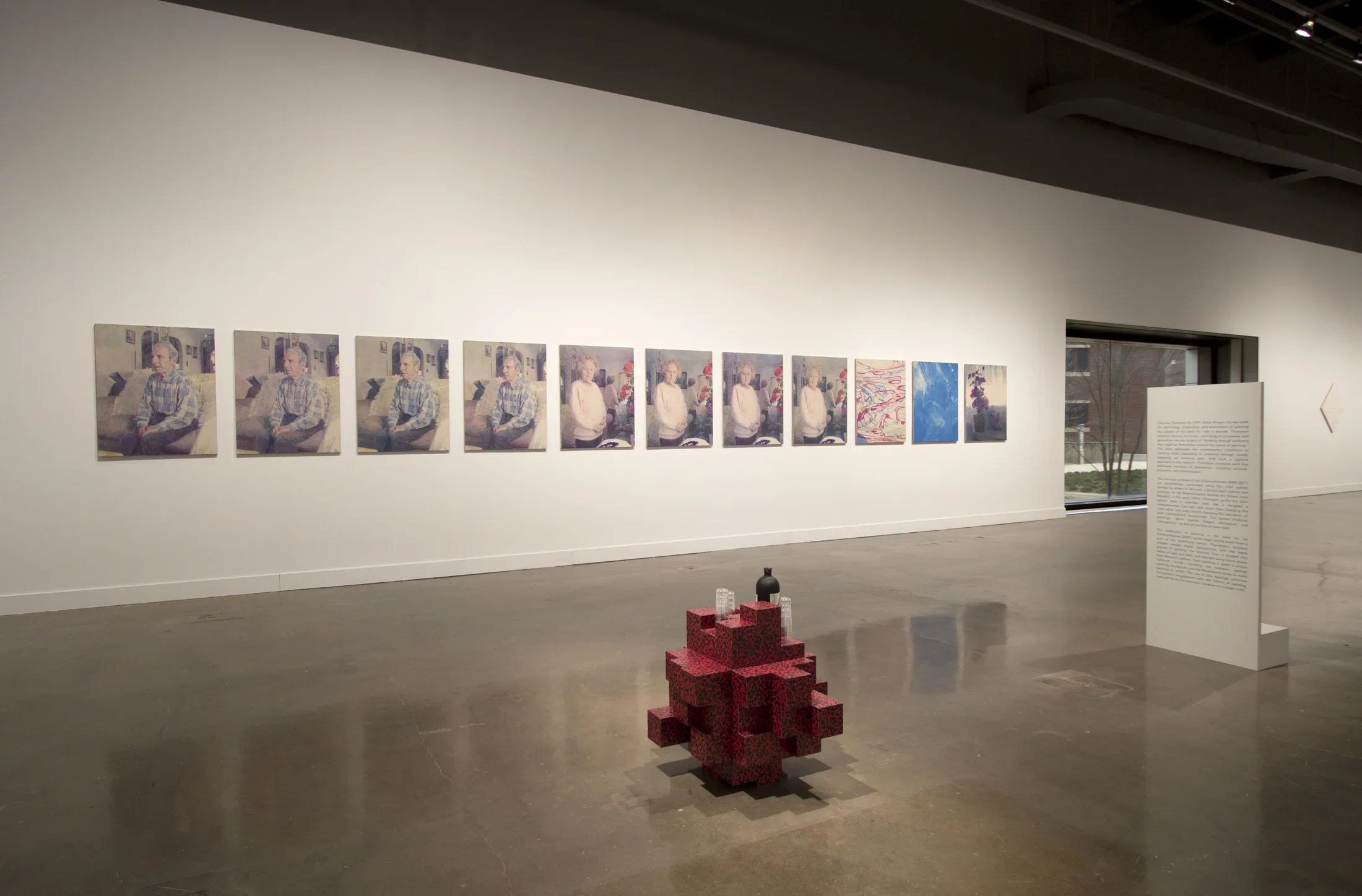 View of gallery with multipanel paintings in the back and red brick sculpture on the ground. 