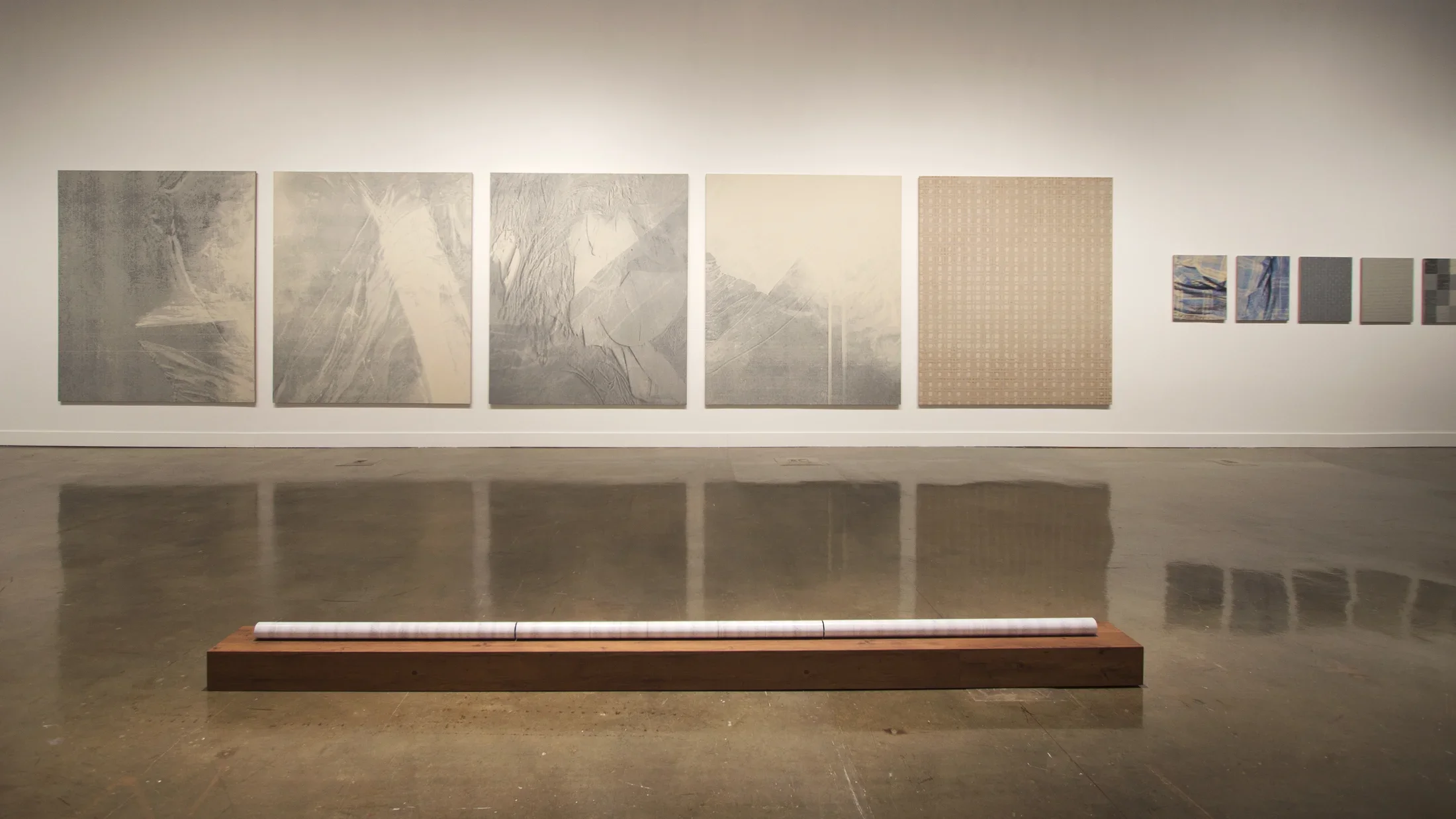 View of gallery with 5 large grey paintings on the left wall and sculptures installed on the floor. 