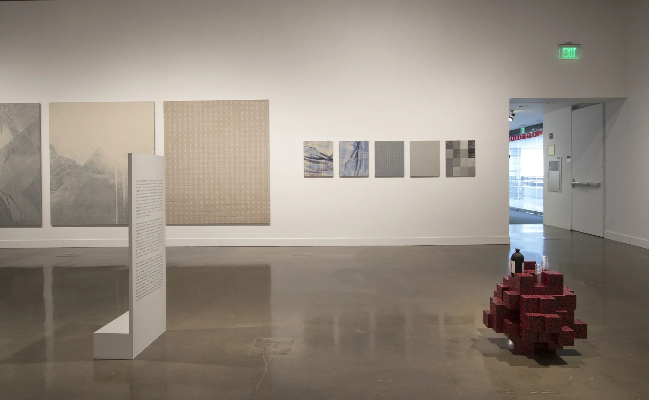 View of gallery with multipanel paintings in the back and red brick sculpture on the ground. 