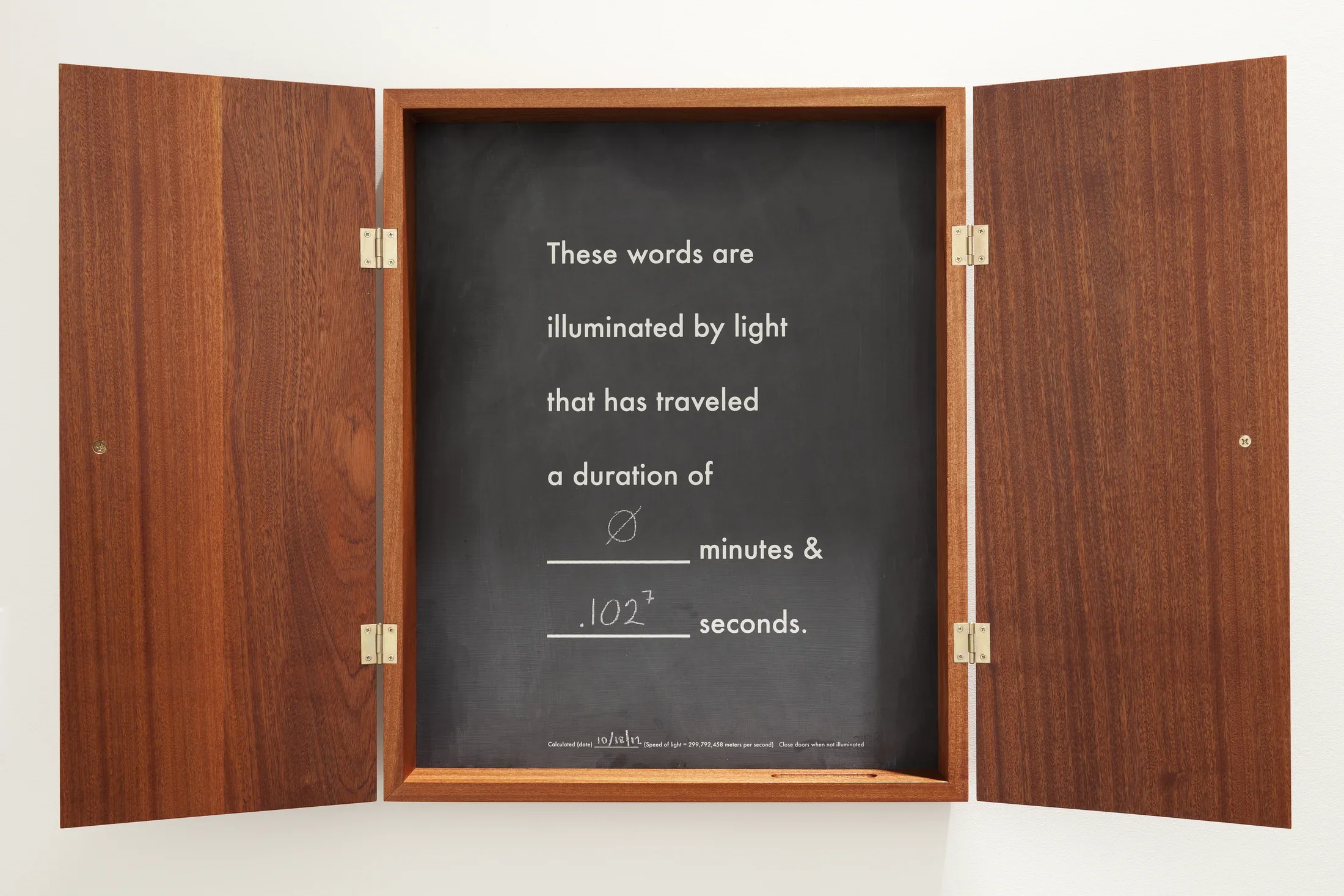 A shallow wood cabinet with chalkboard inset, the words “these words are illuminated by light that has traveled a duration of…”