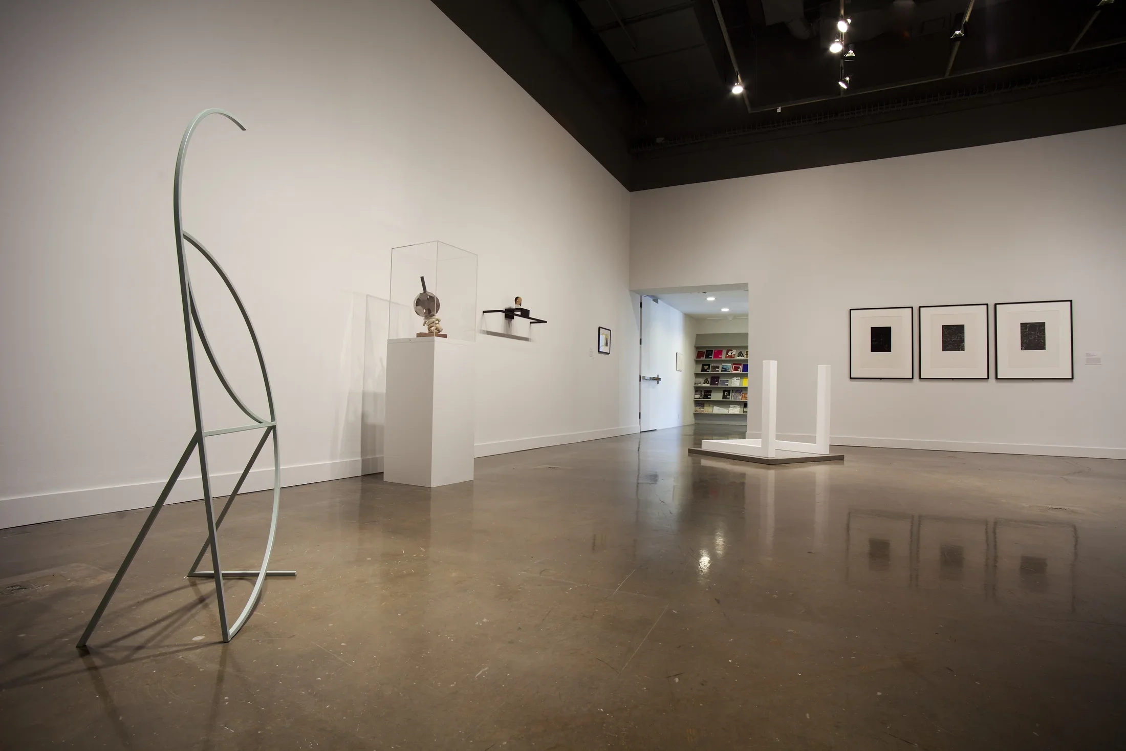 A delicate metal sculpture, a stand with an object, framed pictures and floor sculpture with white base, two white poles