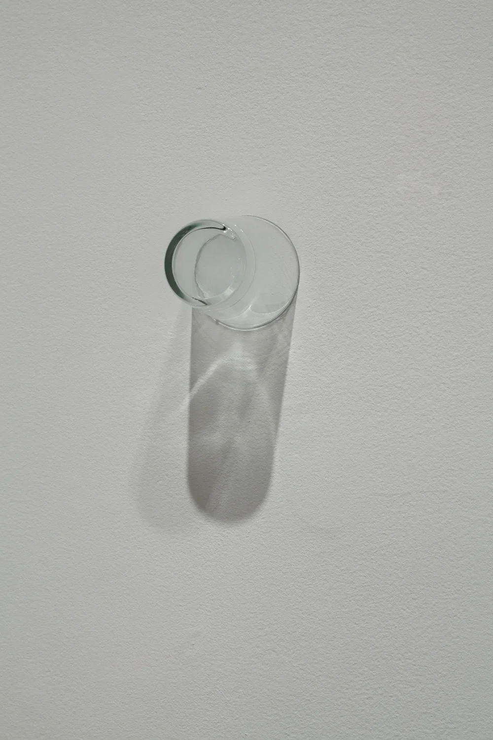  A clear drinking glass is affixed on a wall by its rim.