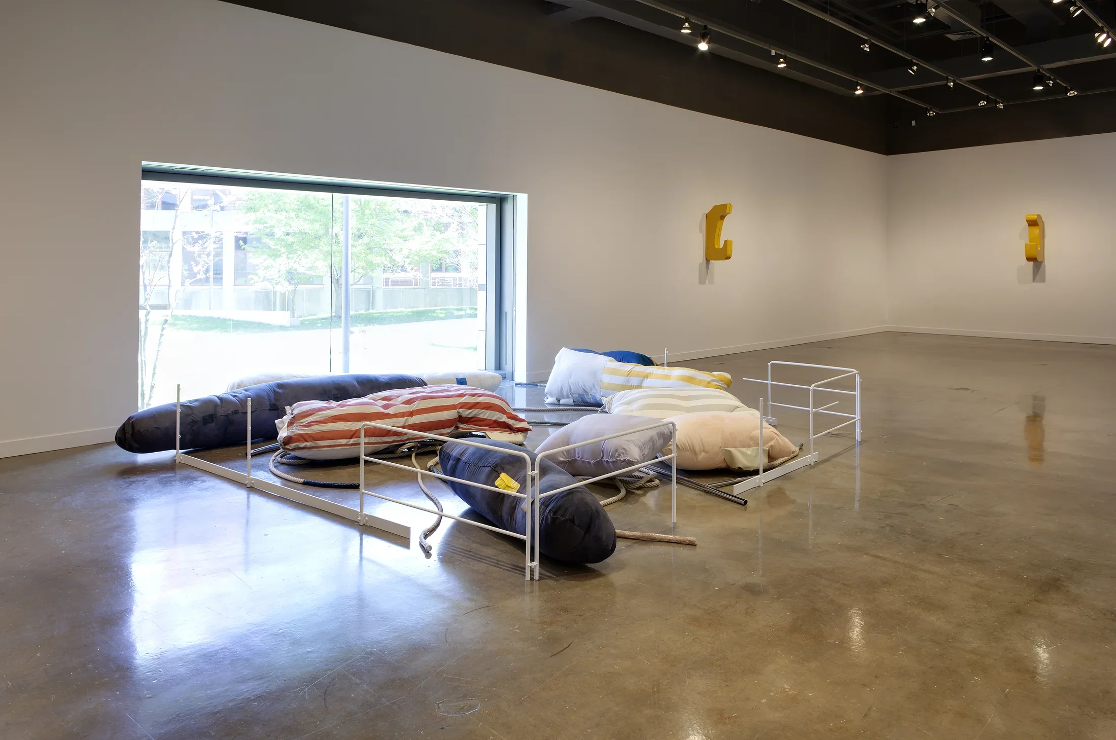 Large pillows of various sizes and colors arranged in front of a large picture window, surrounded on 3 sides by white gates. 