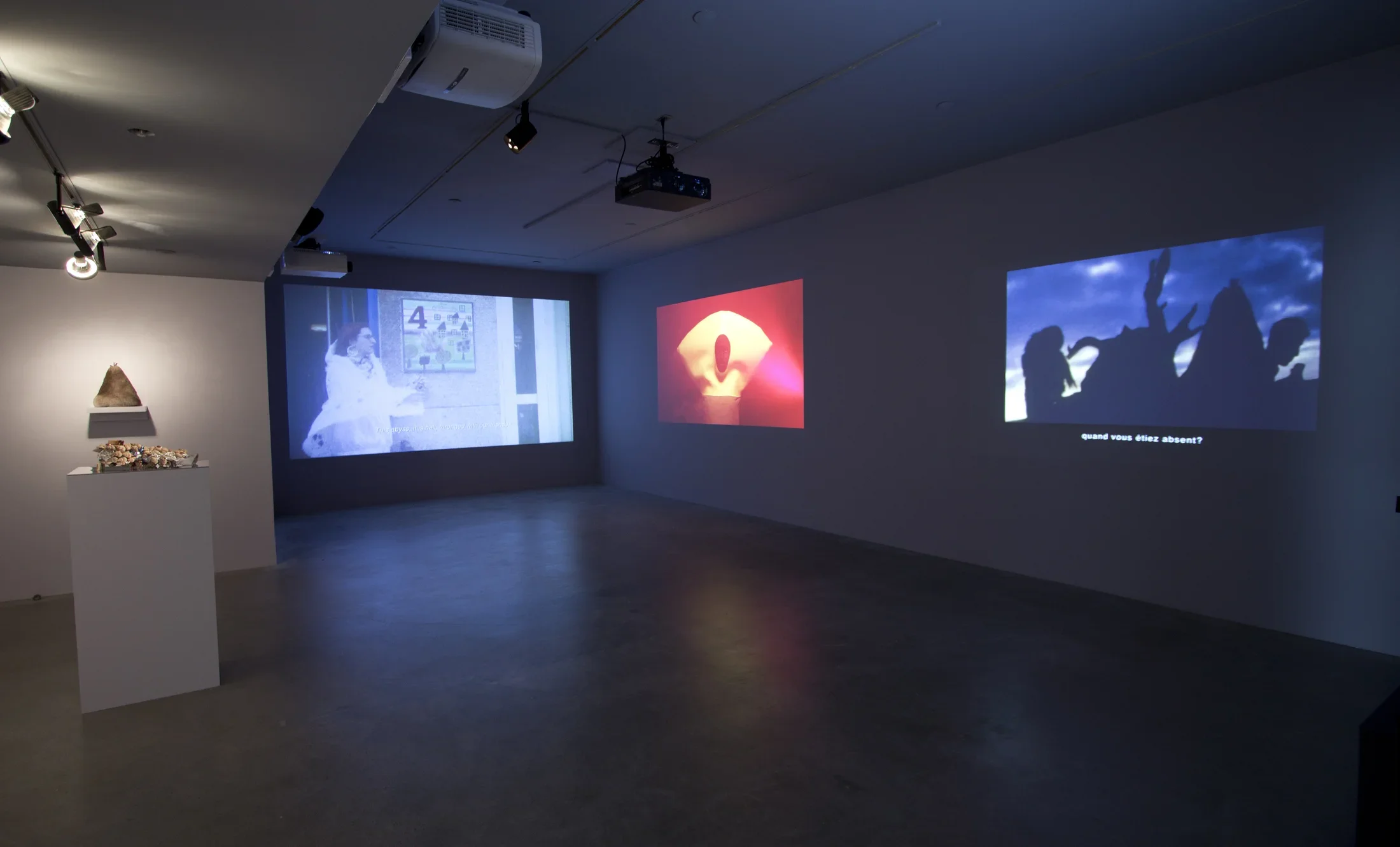 3 large color projections on 2 walls of the gallery next to displays of props