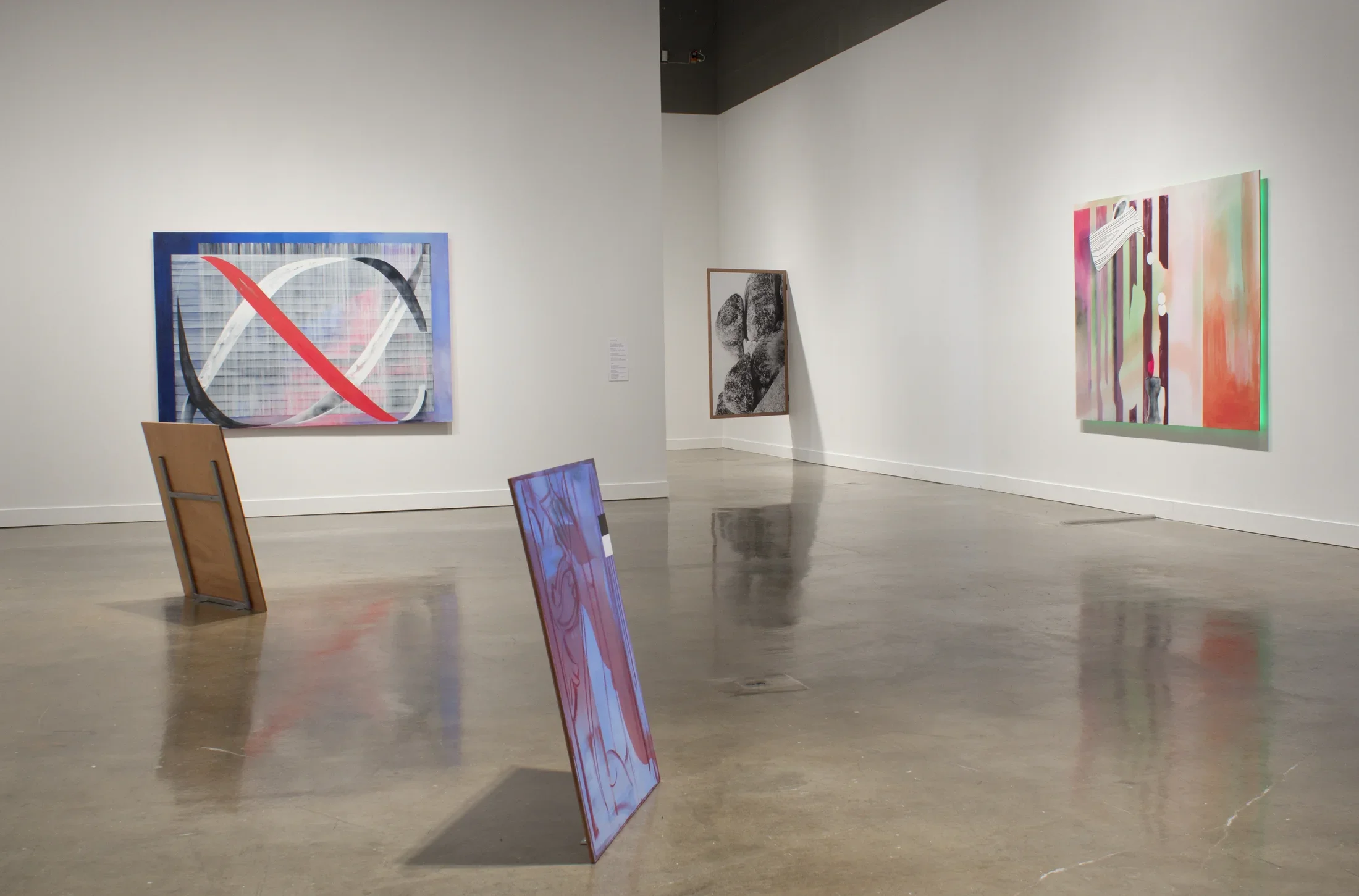 Five paintings are displayed, including 2 on the floor, 2 hung flush against the wall and 1 jutting from the wall.