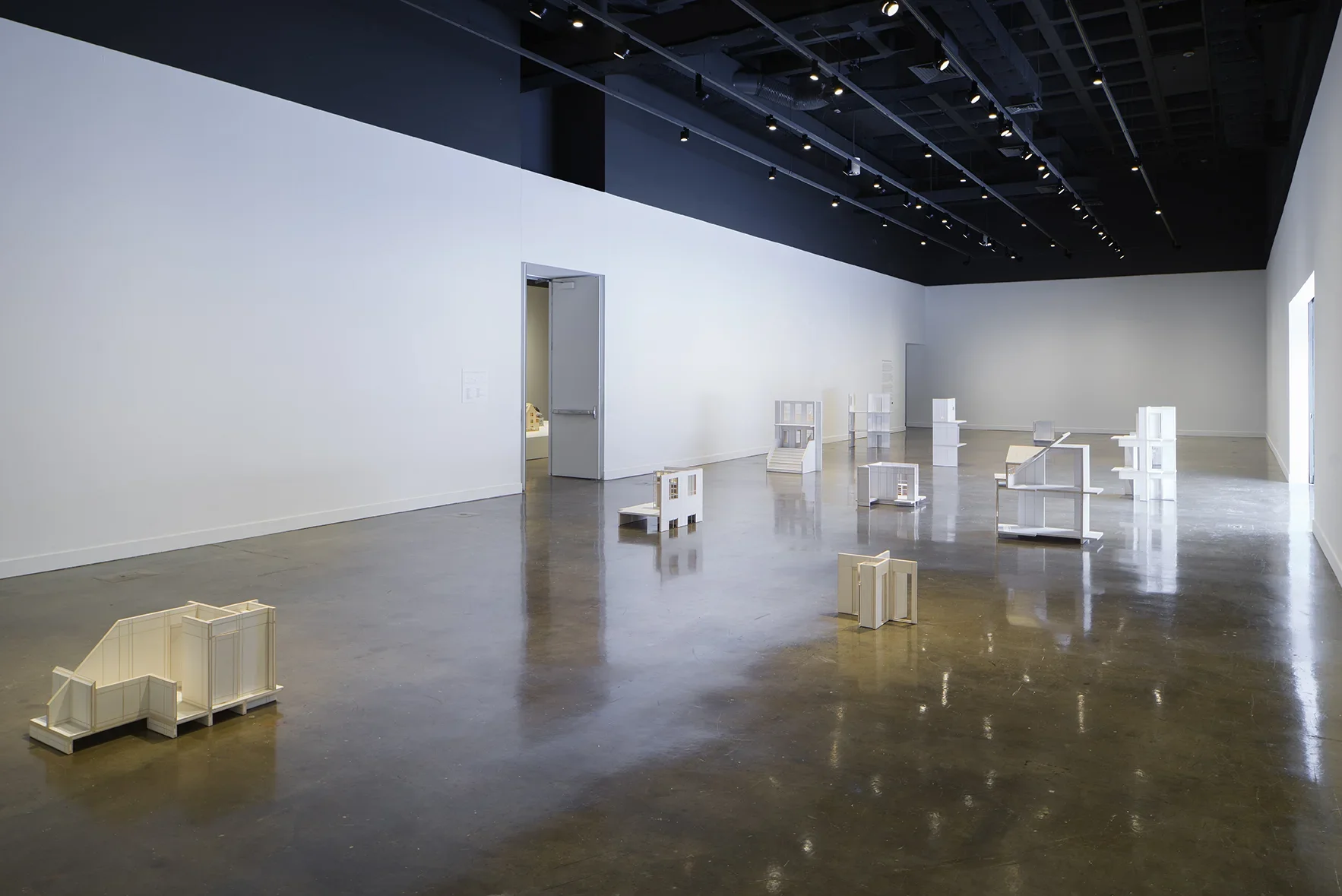 Gallery filled with reflective light and small sculptural objects from afar. 