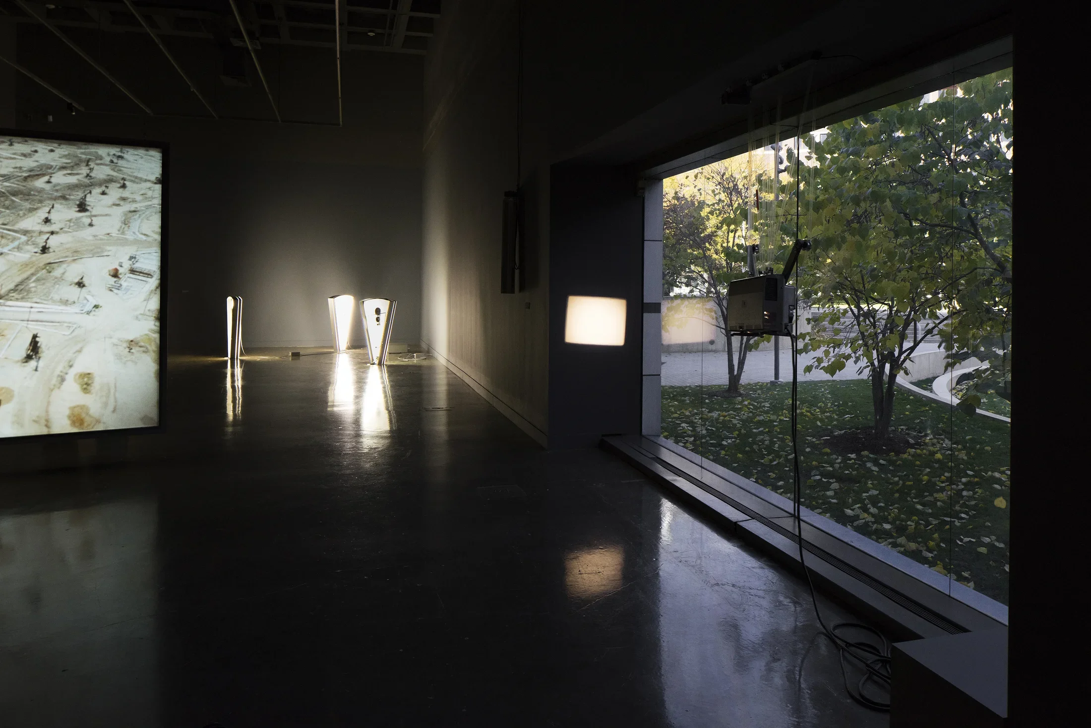 Hanging projector casts a lit rectangle on a wall next to a large window, in the back corner, 3 triangular lit sculptures.