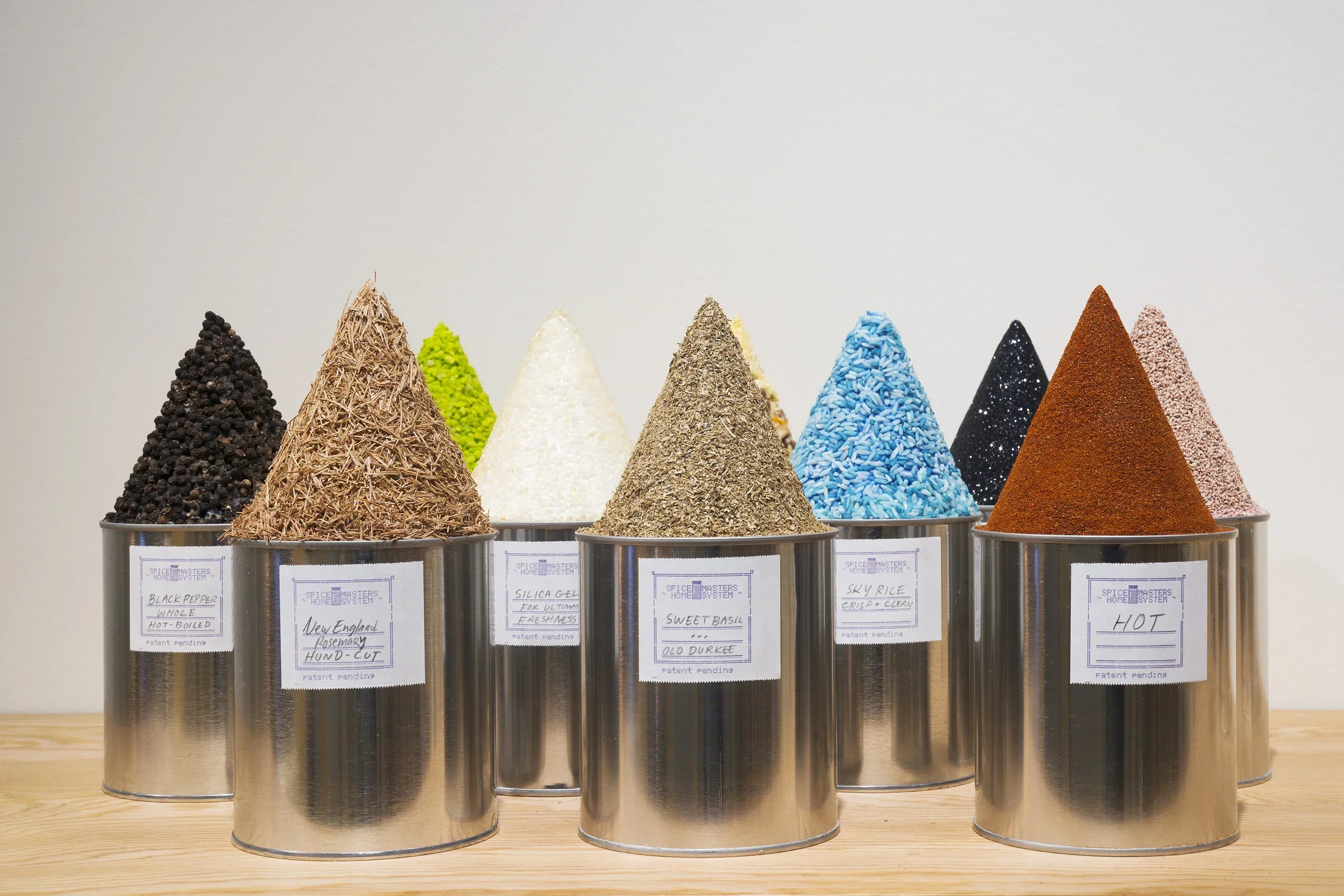 Rows of round tin cans with homemade white labels holding cone shaped mounds of various colored substances and textures
