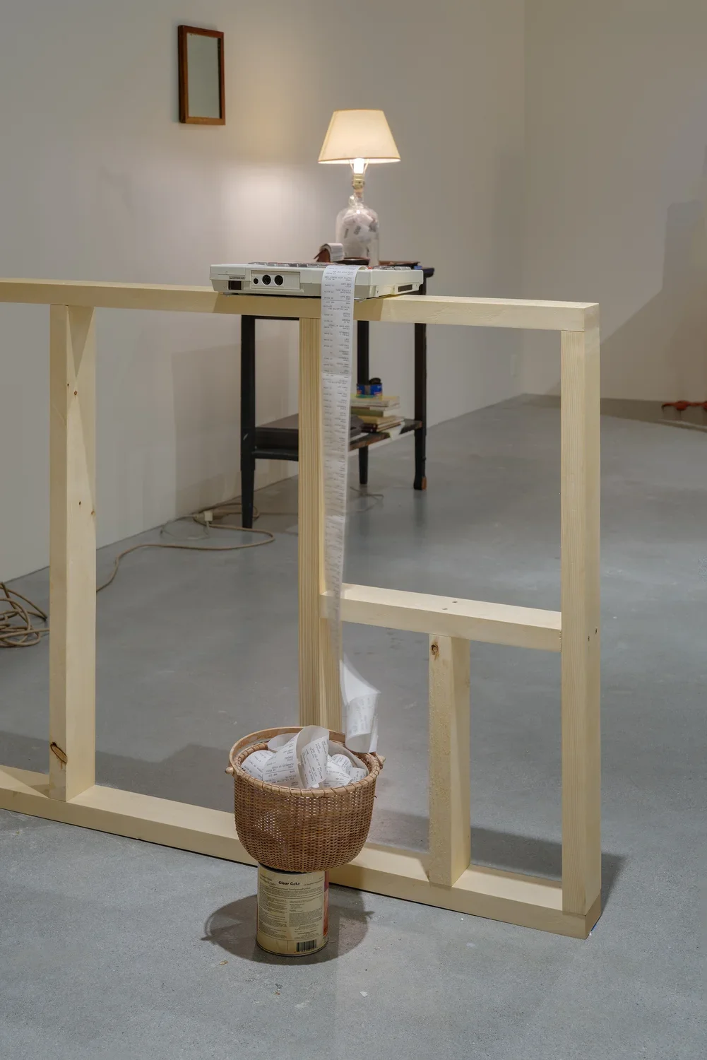A small computer/ printer on a ledge, paper spooled over into a woven basket on top of a paint can, a lighted lamp in back