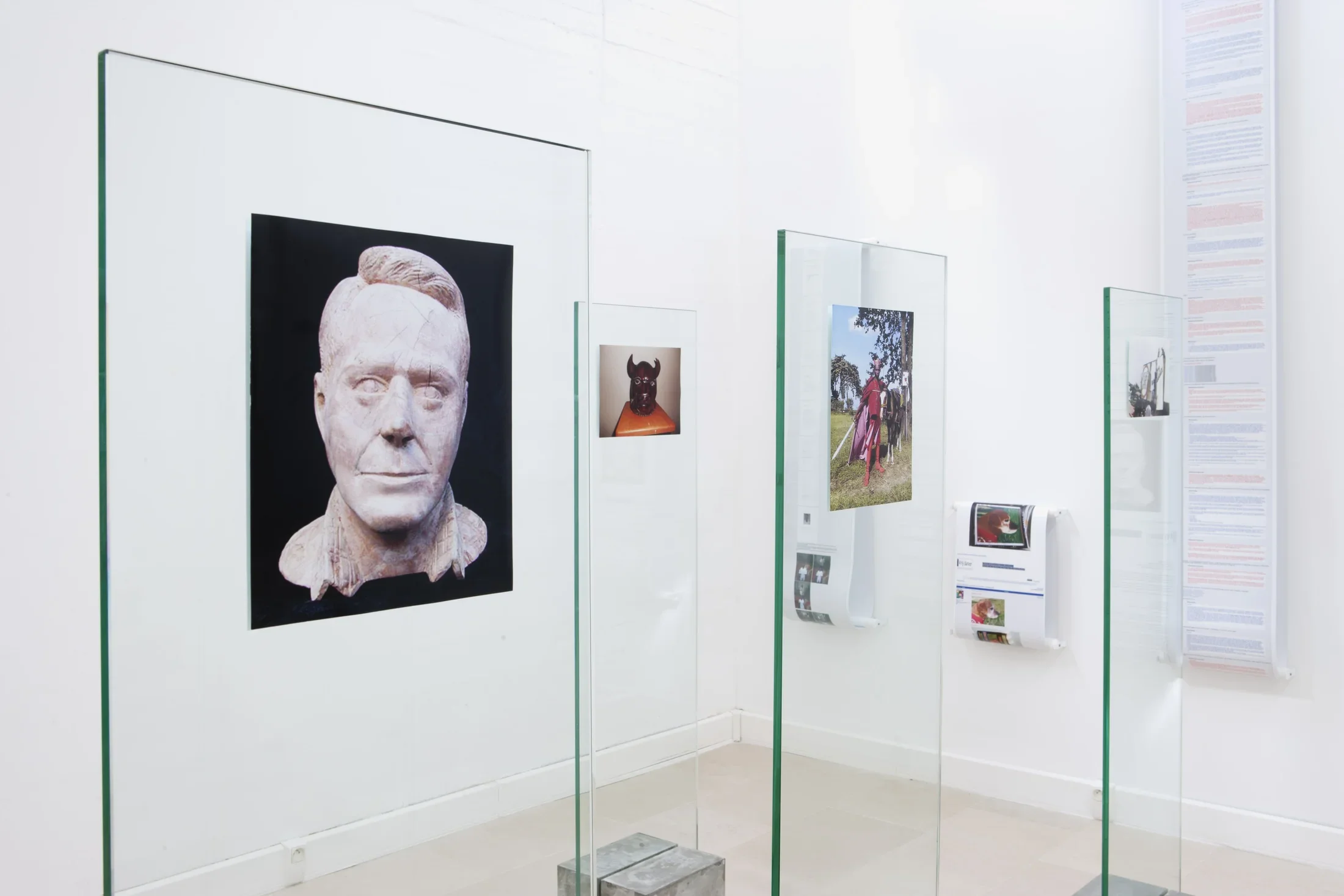 In the foreground, photographs mounted on glass panels, on the back wall, photos and text on rolls hang vertically.