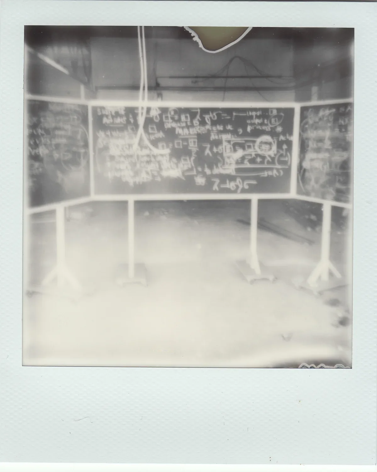 Fogged image of 3 black chalkboards, covered with symbols written in white chalk, in the middle of a dilapidated room
