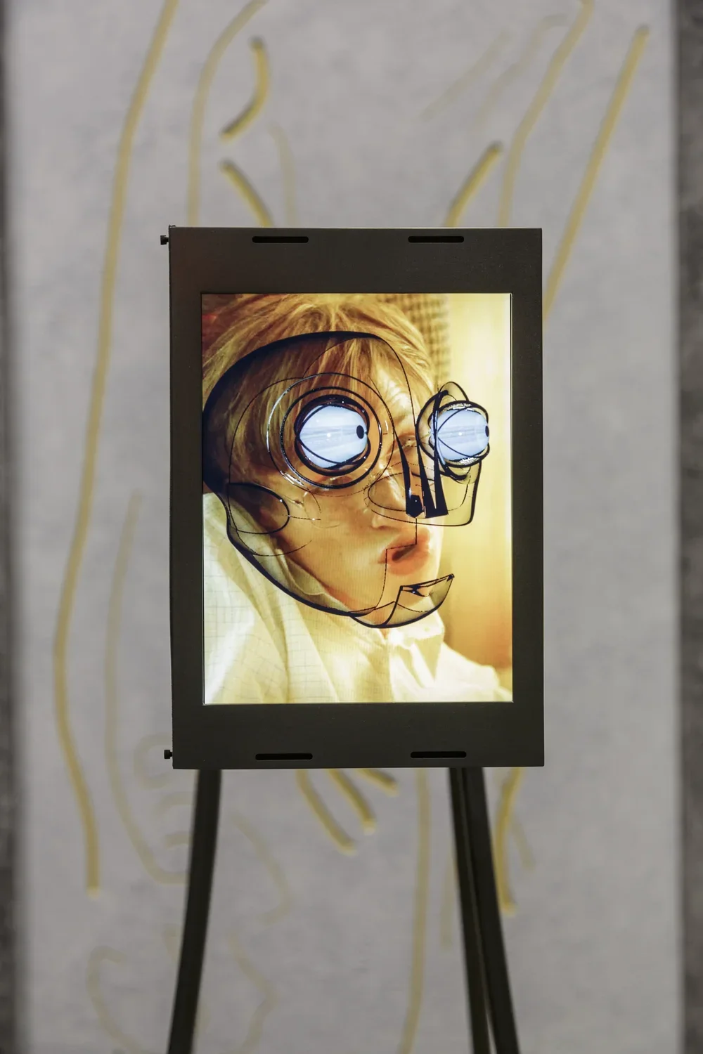 Steel-encased screen shows rendering of robotic face with blue-tinged eye bulbs superimposed on a distorted human face.