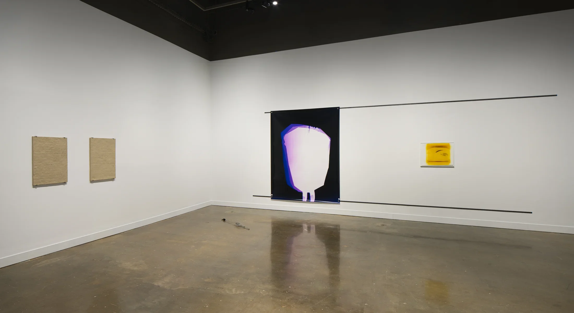 A corner space, two clay tablets on left wall, a large abstract print and a small yellow and black print on wall to the right