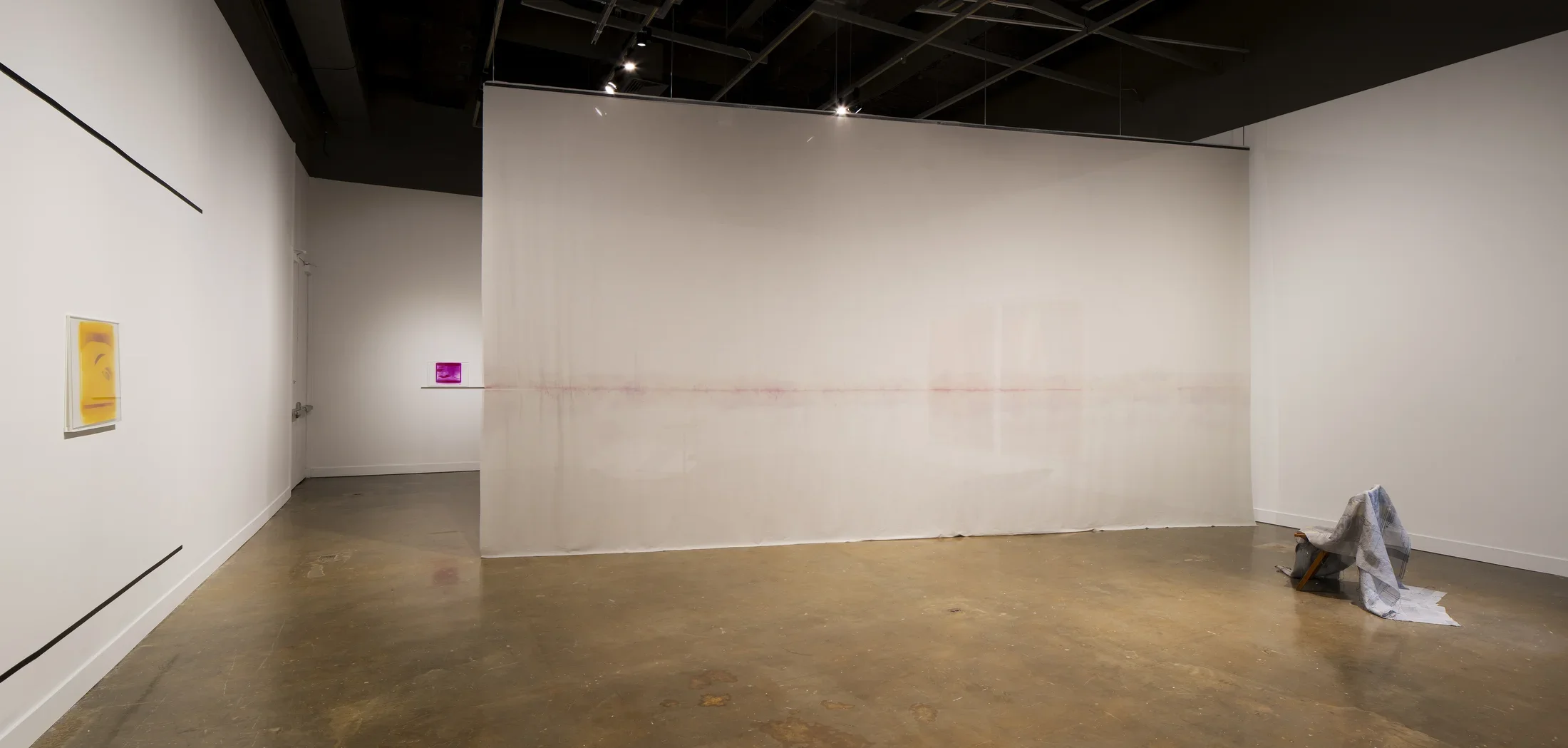 Installation view of a space with a large hanging cloth, two small prints, a yellow and a purple, a cloth folded over a chair