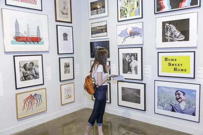 Student in gallery filled floor to ceiling with artworks.
