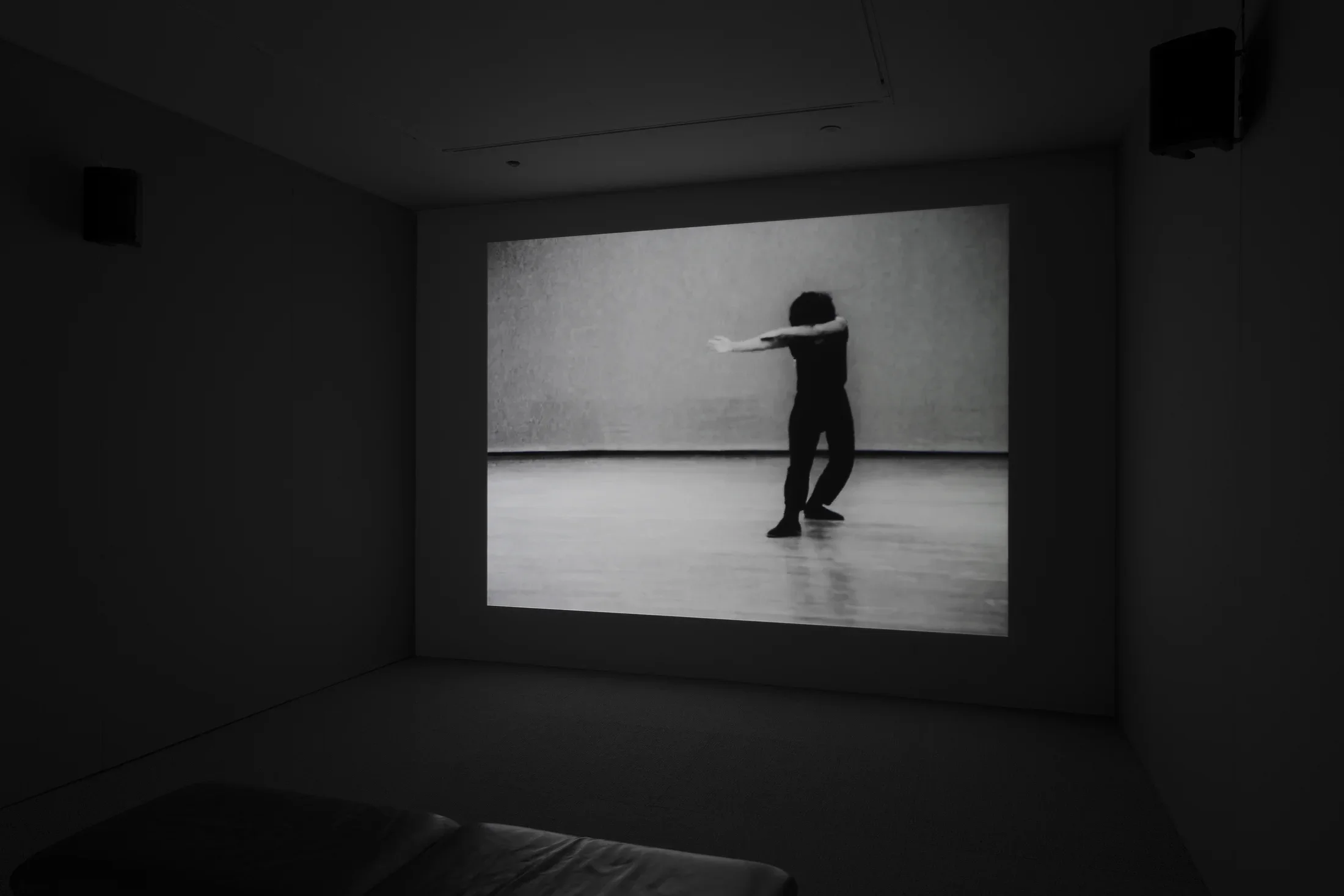 Video display of a dancer in black, posed with head bowed, both arms stretched out to her right, with right leg forward.