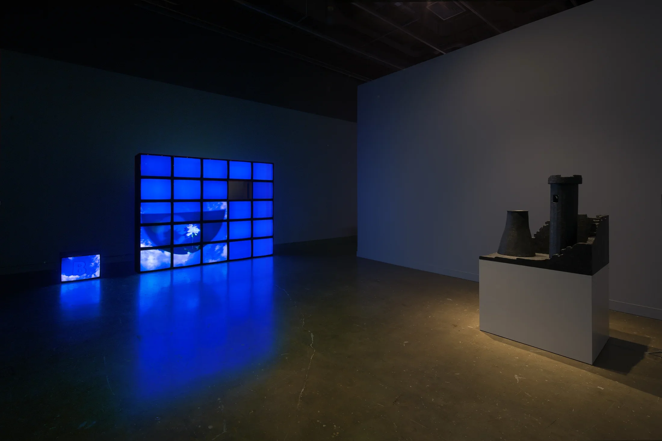 A wall of video monitors display an overall blue image, castle tower with a nuclear stack sits on a pedestal in front.