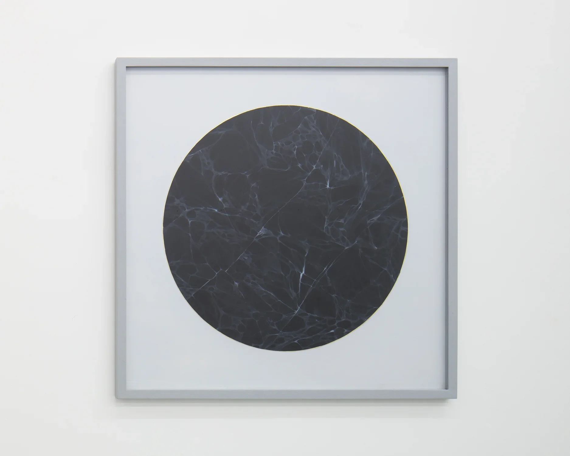 Gray square frame surrounds painting of a circle of black veined marble outlined with gold leaf on paper.