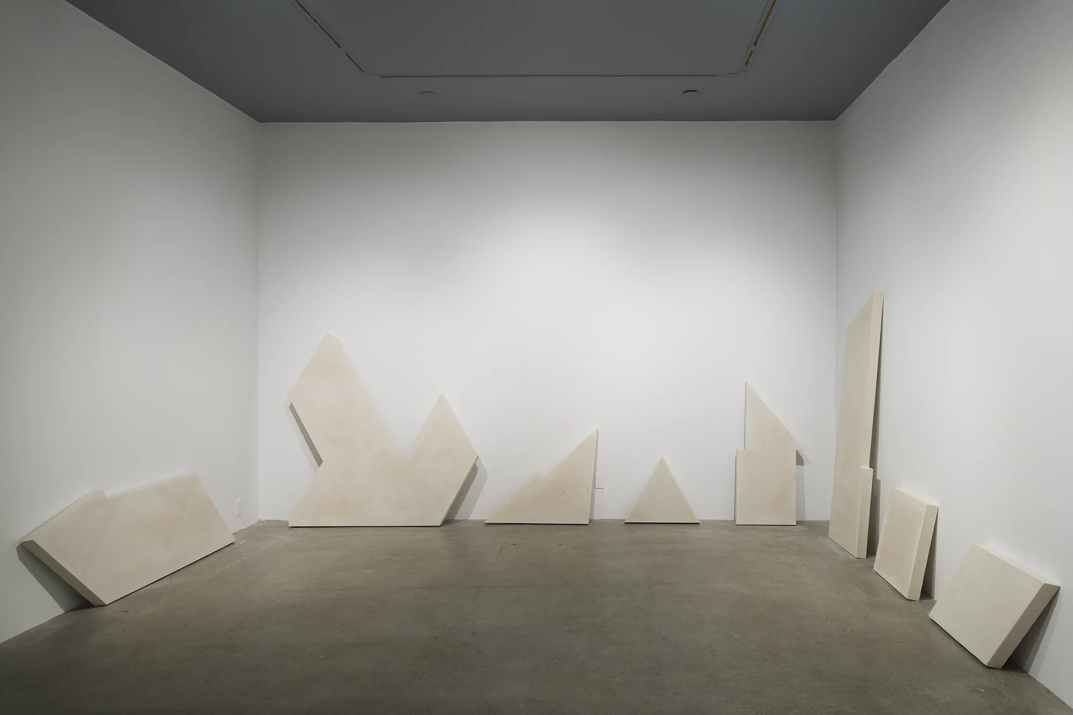 Irregularly shaped cast concrete panels of differing sizes line 3 blank walls of a gallery space.